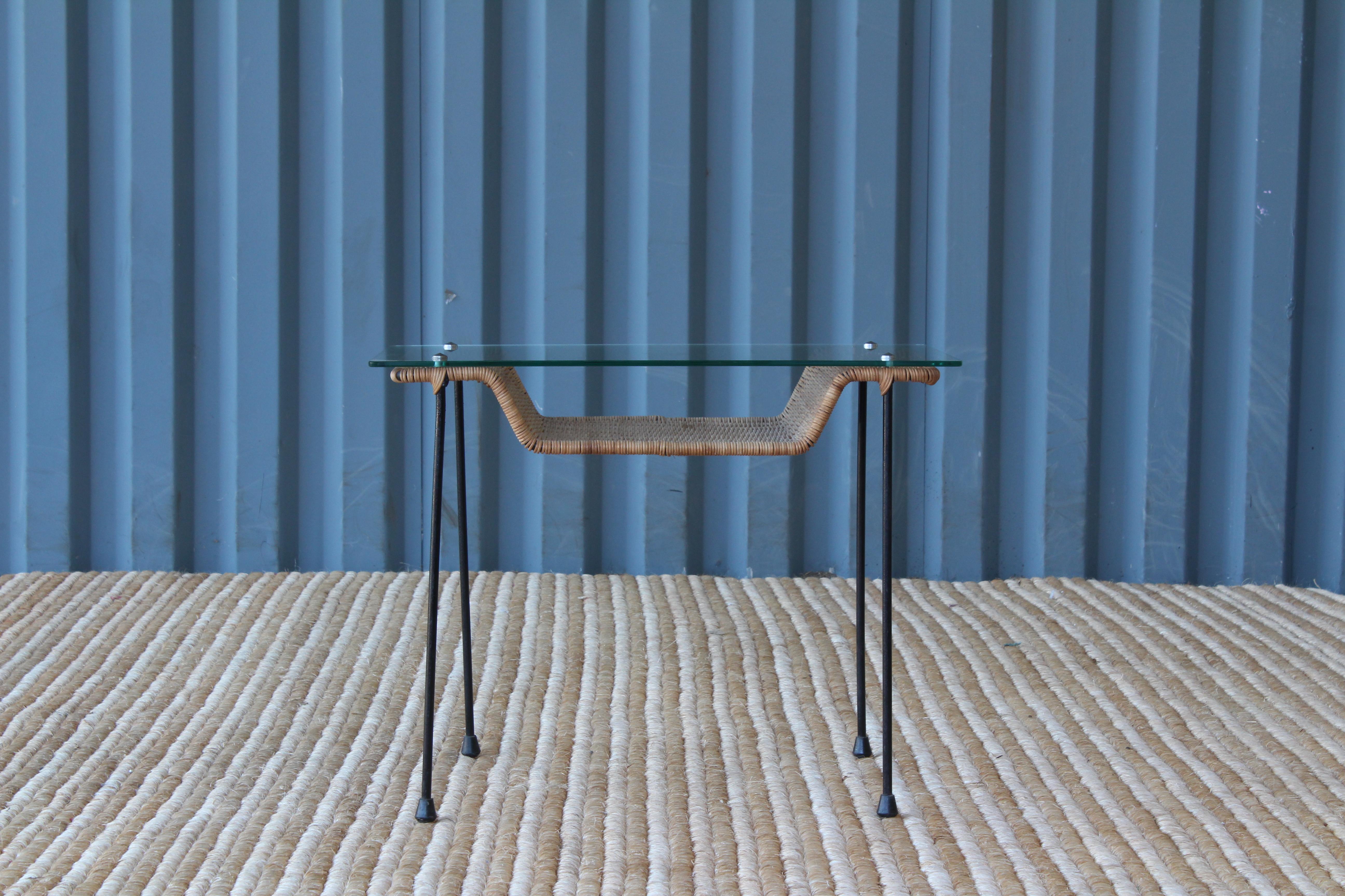Petite iron side table with a rattan shelf and glass surface.