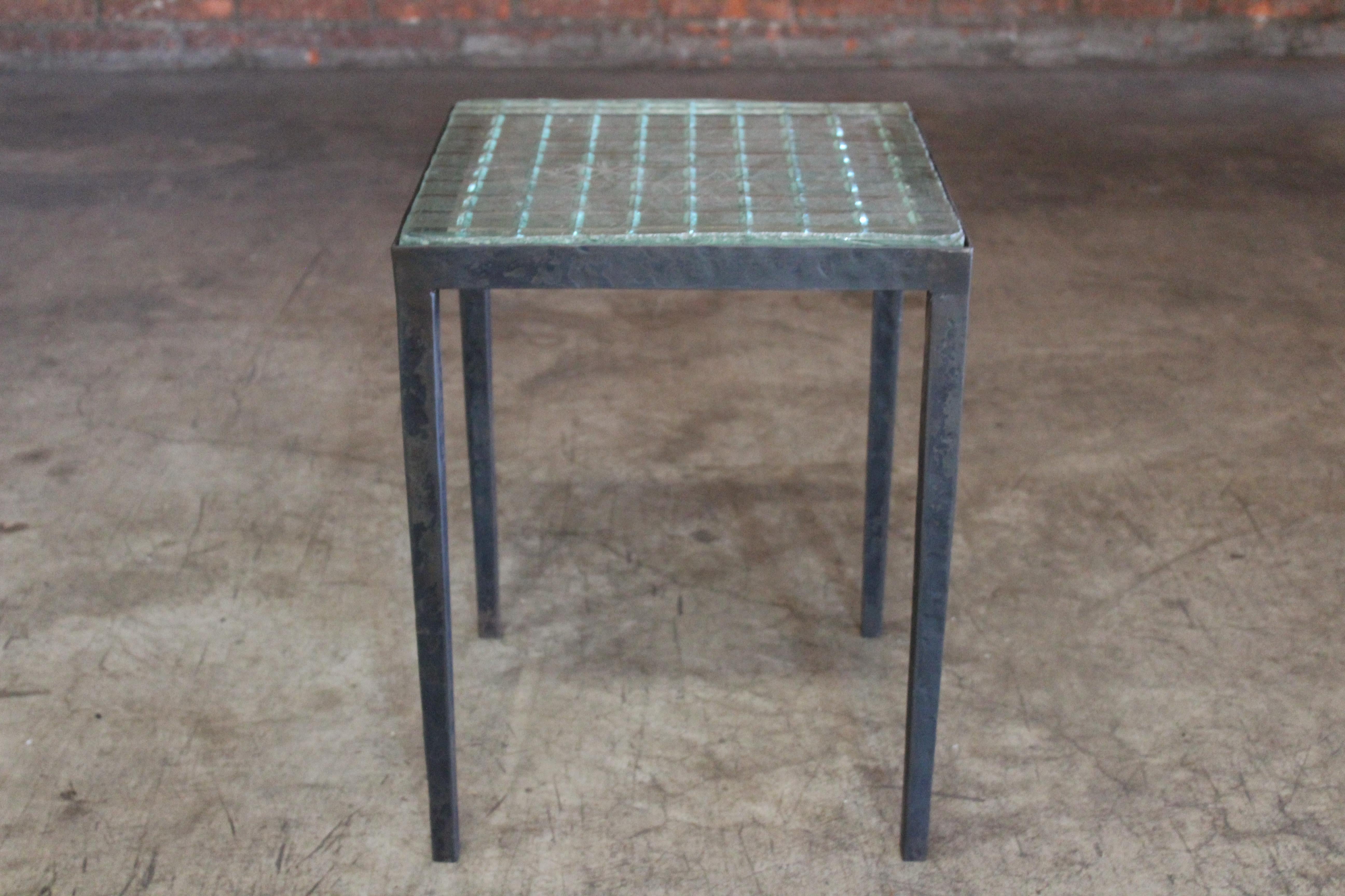 An iron side table with a vintage 1930s Saint-Gobain glass inserted top. In the manner of Jean-Michel Frank. In good condition. The iron base is forged with hammered details in a blackened steel finish. The glass top shows minor chips and wear along