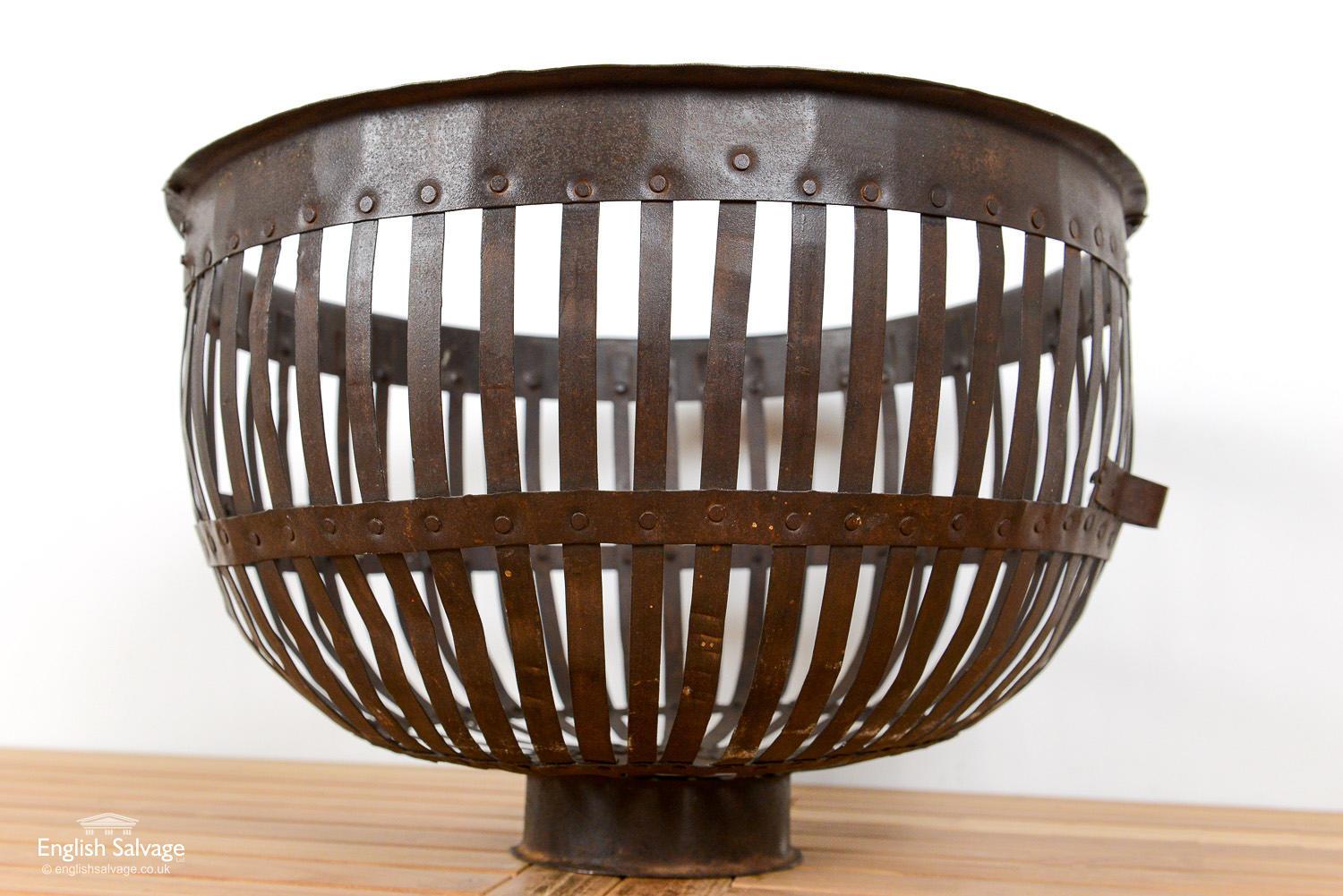 Reclaimed large iron basket with slatted sides, studded detailing around the rim and two bands below. The storage basket has two small handles and is set on a smaller circular base. Some tarnishing and wear due to past use.