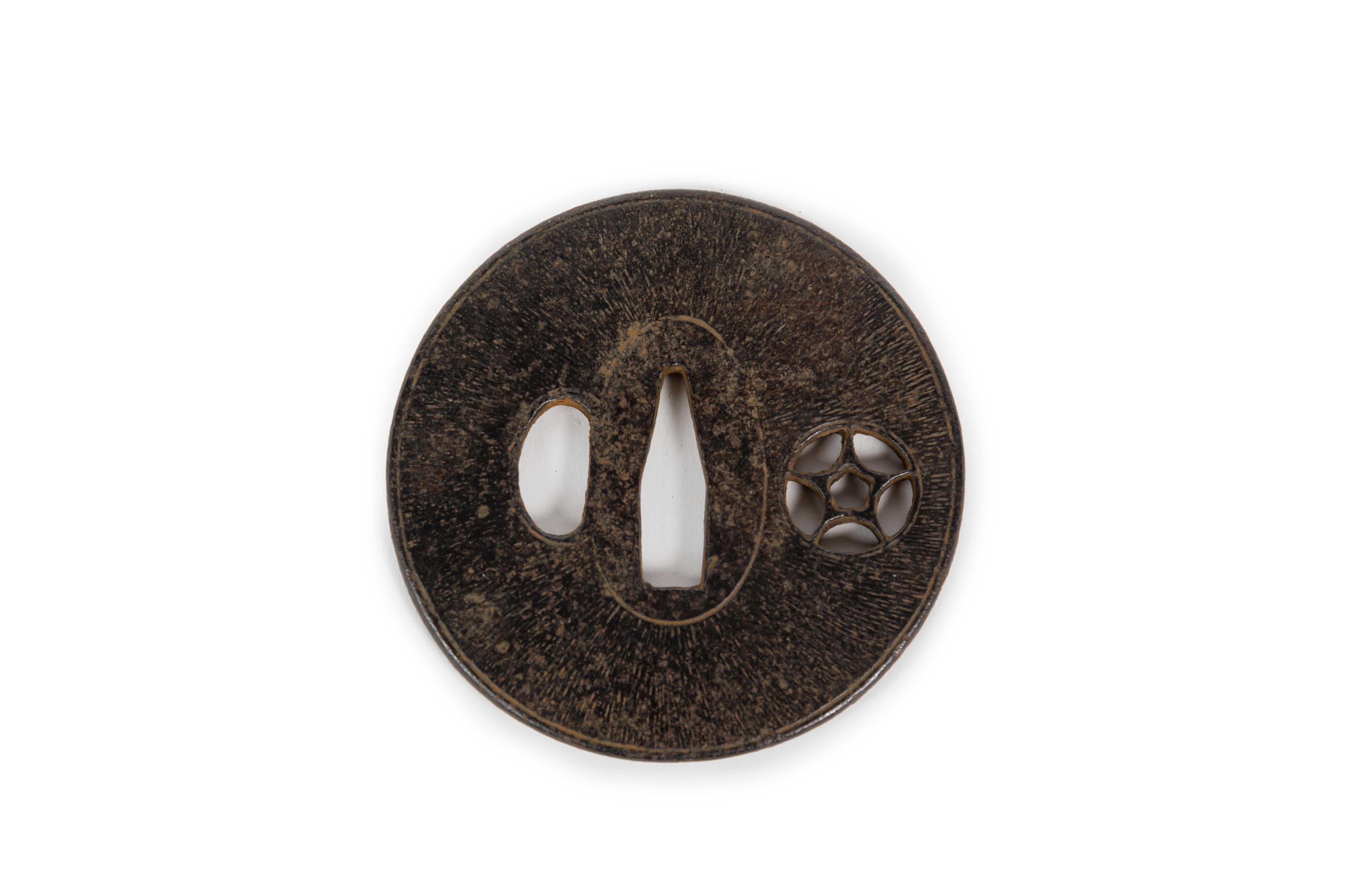 Elegant tsuba in forged iron, with a textured pattern imitating wood grain, also decorated with an openwork motif of a flower within a star, likely a mon (family crest). The tsuba is a component of the traditional Japanese sword; together with the
