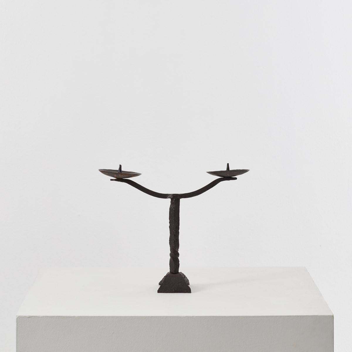 Made from iron, this two-armed candelabra has a subtle grandeur. The rough raw iron surface contrasts the grandeur of the candelabra.
