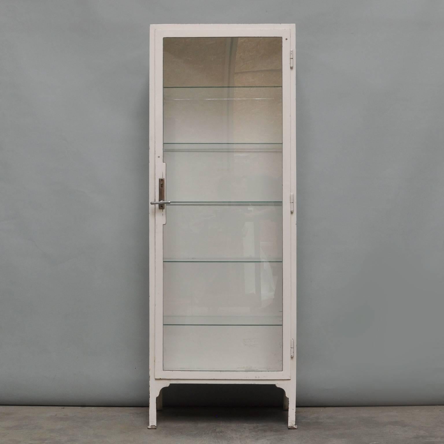 This vintage cabinet was produced in Austria during the 1940s. The cabinet is made of thick steel and comes with five glass shelves. The glass of the cabinet is antiqued. The item has a original lock. It is in a nice vintage condition, missing some