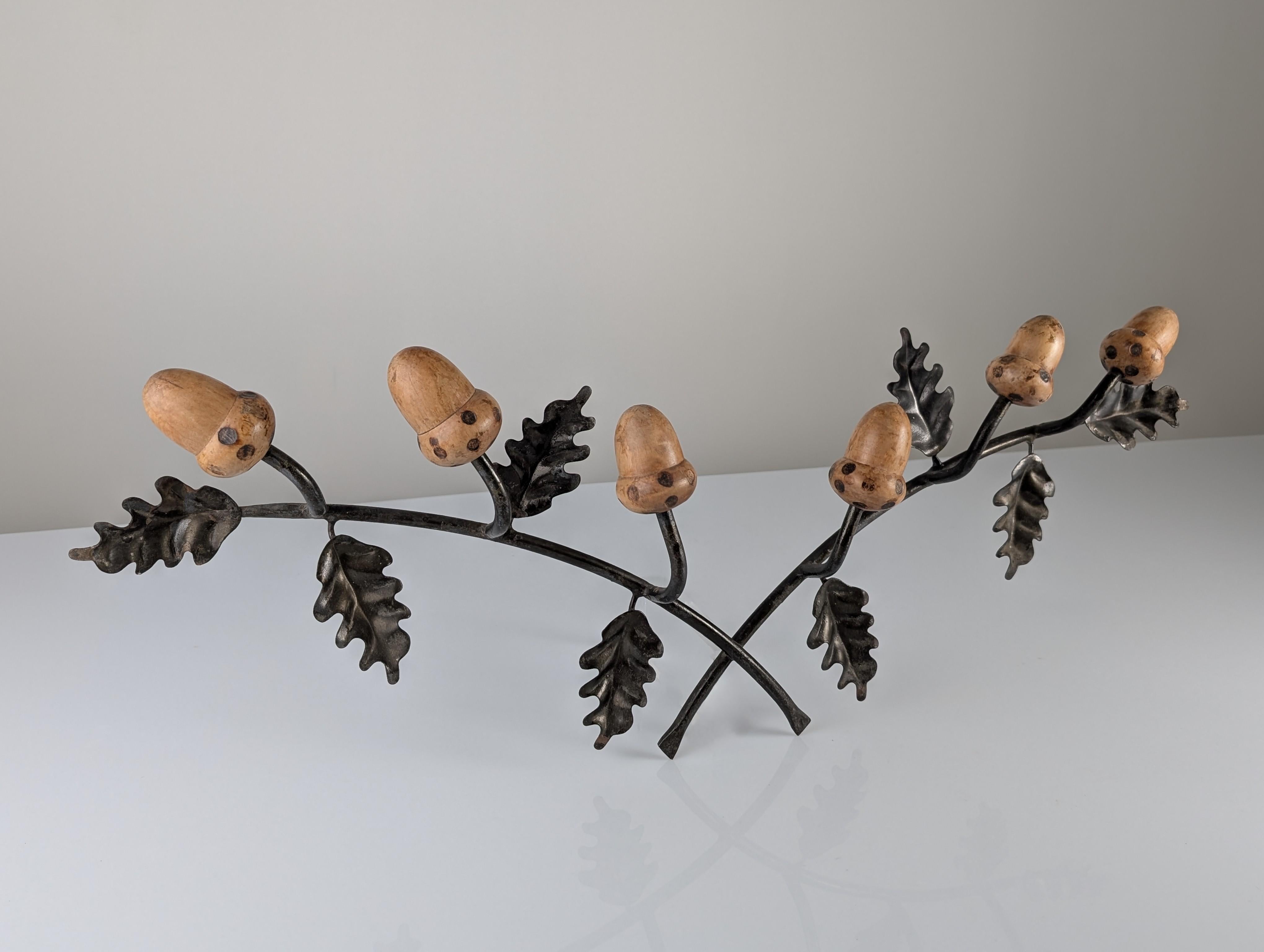 This mid-century wall coat rack is a sculptural piece that merges wrought iron with the warmth of wood. The design is inspired by nature, featuring detailed Holm Oak branches in wrought iron, whose dark finish contrasts with the acorns carved in