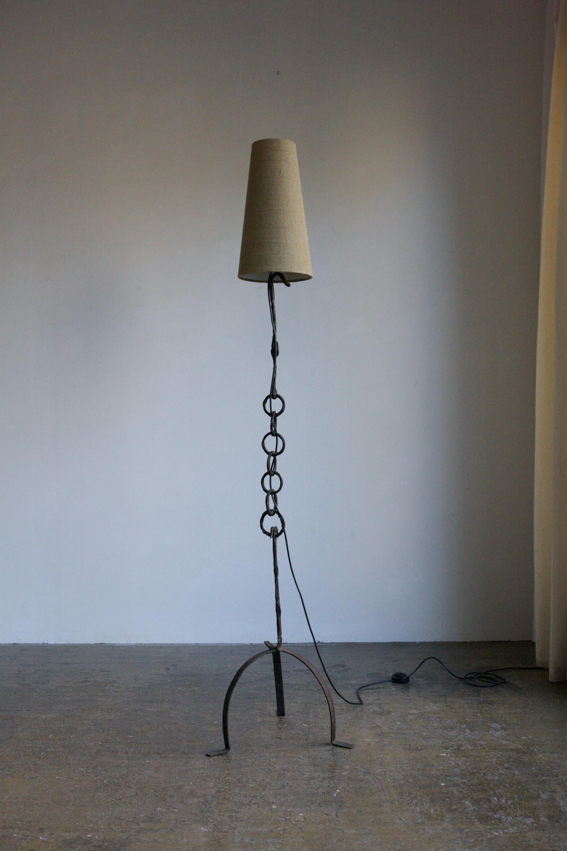 A tall floor lamp in wrought iron with a fused chain detail. Circa 1960's France and likely made by an artisan. Finished with a linen lamp shade. 