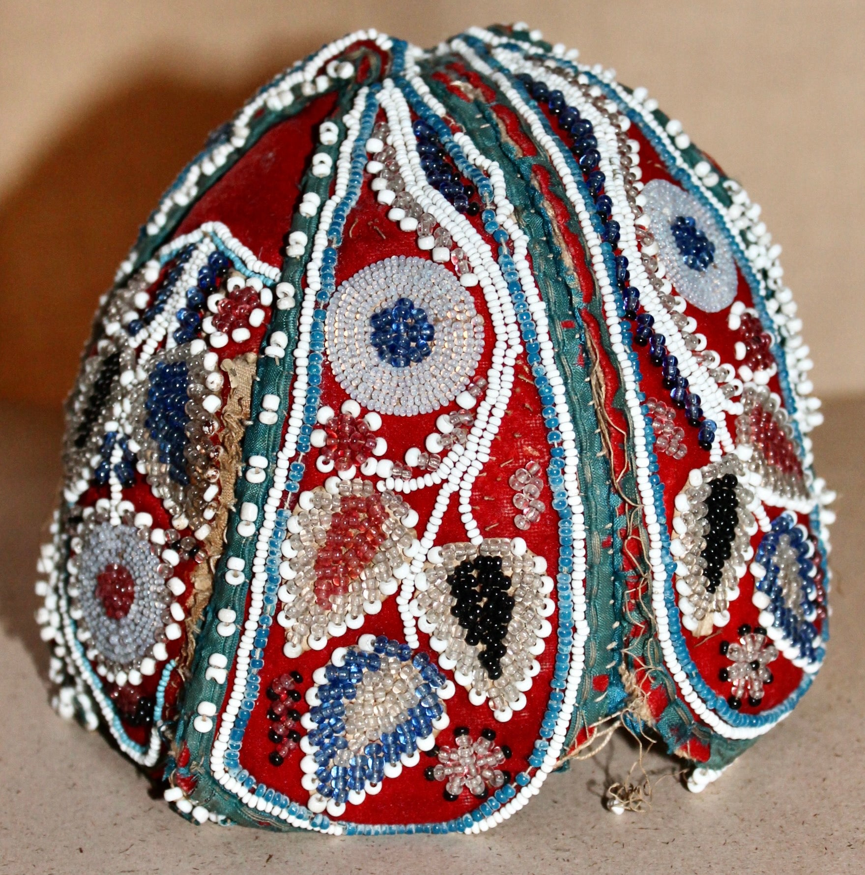 An Iroquois child's cap, beautiful floral designs in multi-colored beads woven on red fabric.