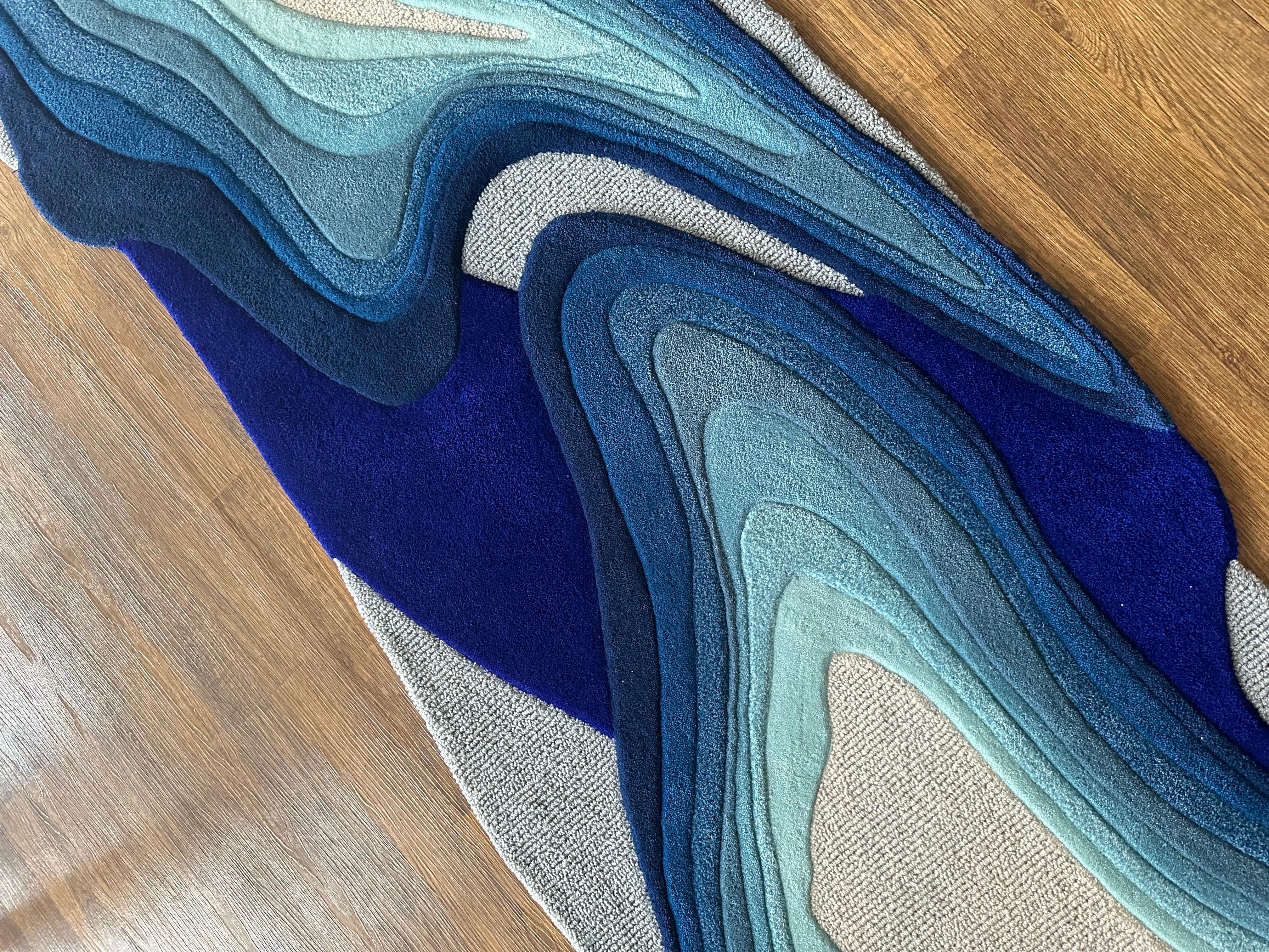 Tufted as a custom long runner with gradients transitioning from cobalt blue to grey, this contemporary rug encapsulates nature's excerpts—frozen bubbles of Abraham Lake, ocean waves, water ripples, and iceberg formations—transformed into an
