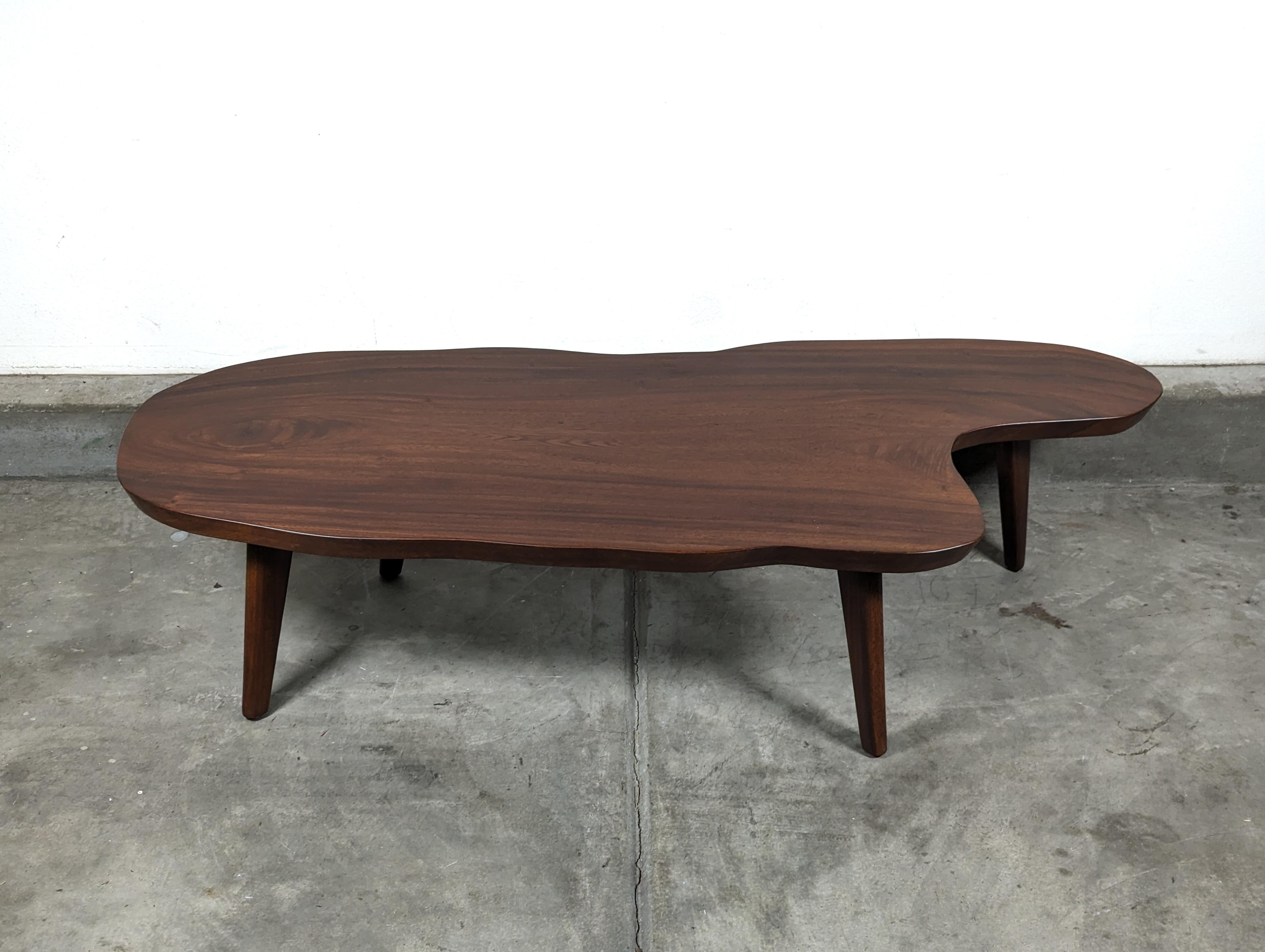 Nestled within the confines of your living space, this exquisite mid-century modern coffee table, circa 1970s, becomes an immediate conversation piece. Crafted from a single, solid slab of the enchanting monkey pod wood, likely sourced from the lush
