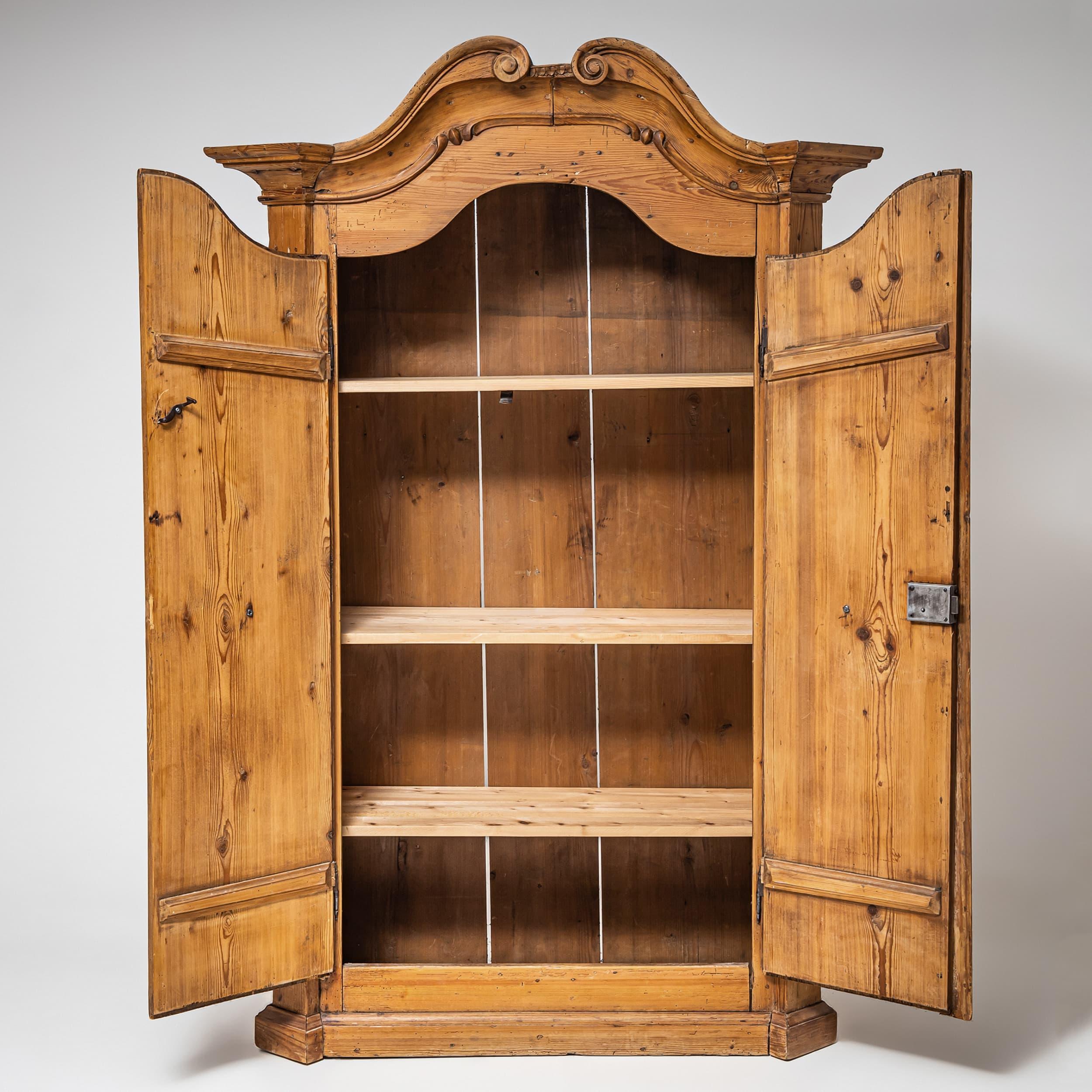 Armadio barocco a due ante della regione di Irschenberg, risalente al XVIII secolo. Realizzato in legno massiccio di conifera con una patina calda e invecchiata. Le porte sono strutturate con pannelli scolpiti e curvilinei e ferramenta in ferro e