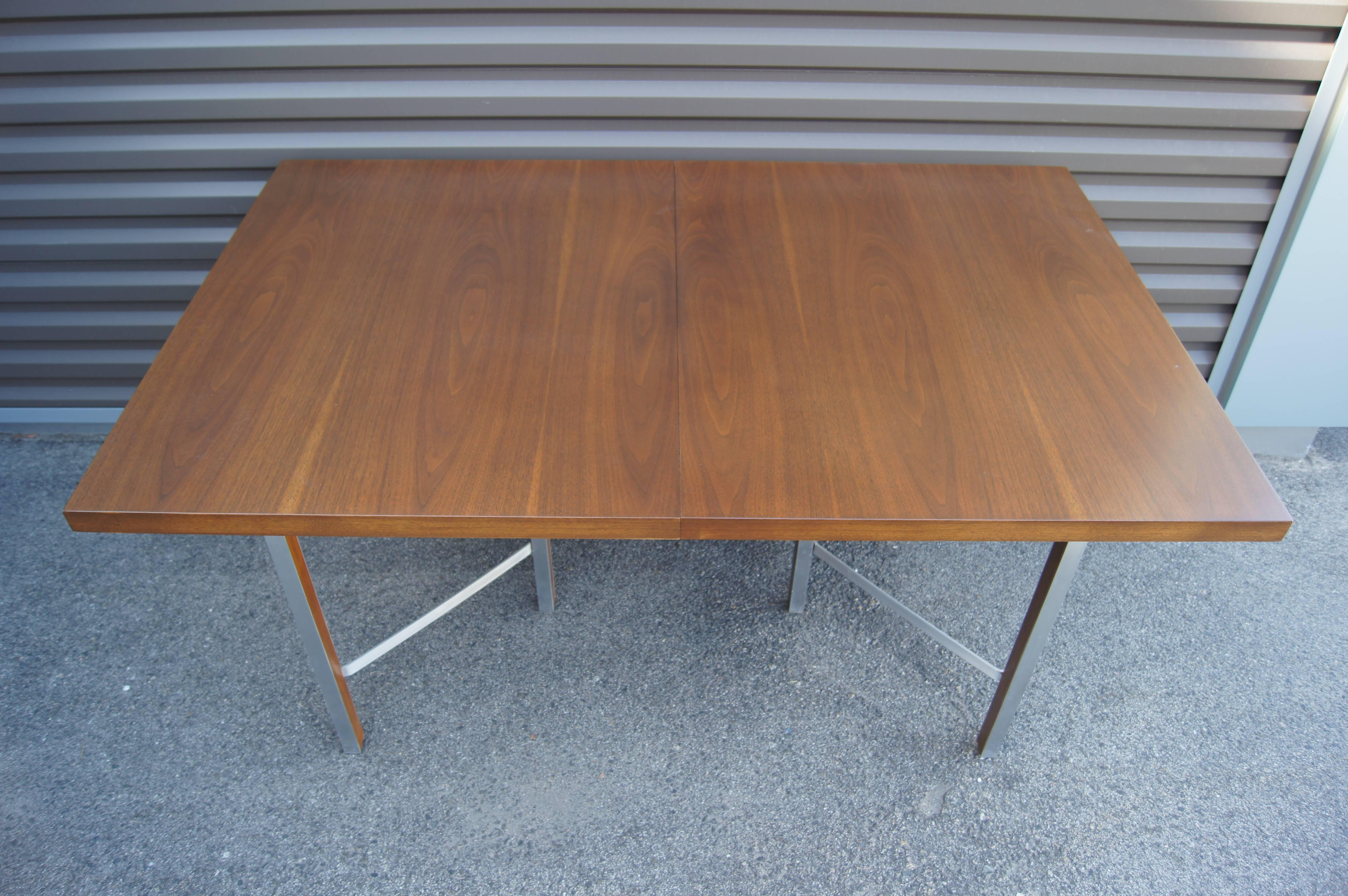 Paul McCobb hat diesen markanten Esstisch als Teil seiner Irwin Group Collection für Calvin Furniture entworfen. Die Platte aus Nussbaumholz ruht auf schlanken, gewinkelten Aluminiumbeinen. Mit zwei 15-Zoll-Blättern lässt sich der Tisch auf bis zu