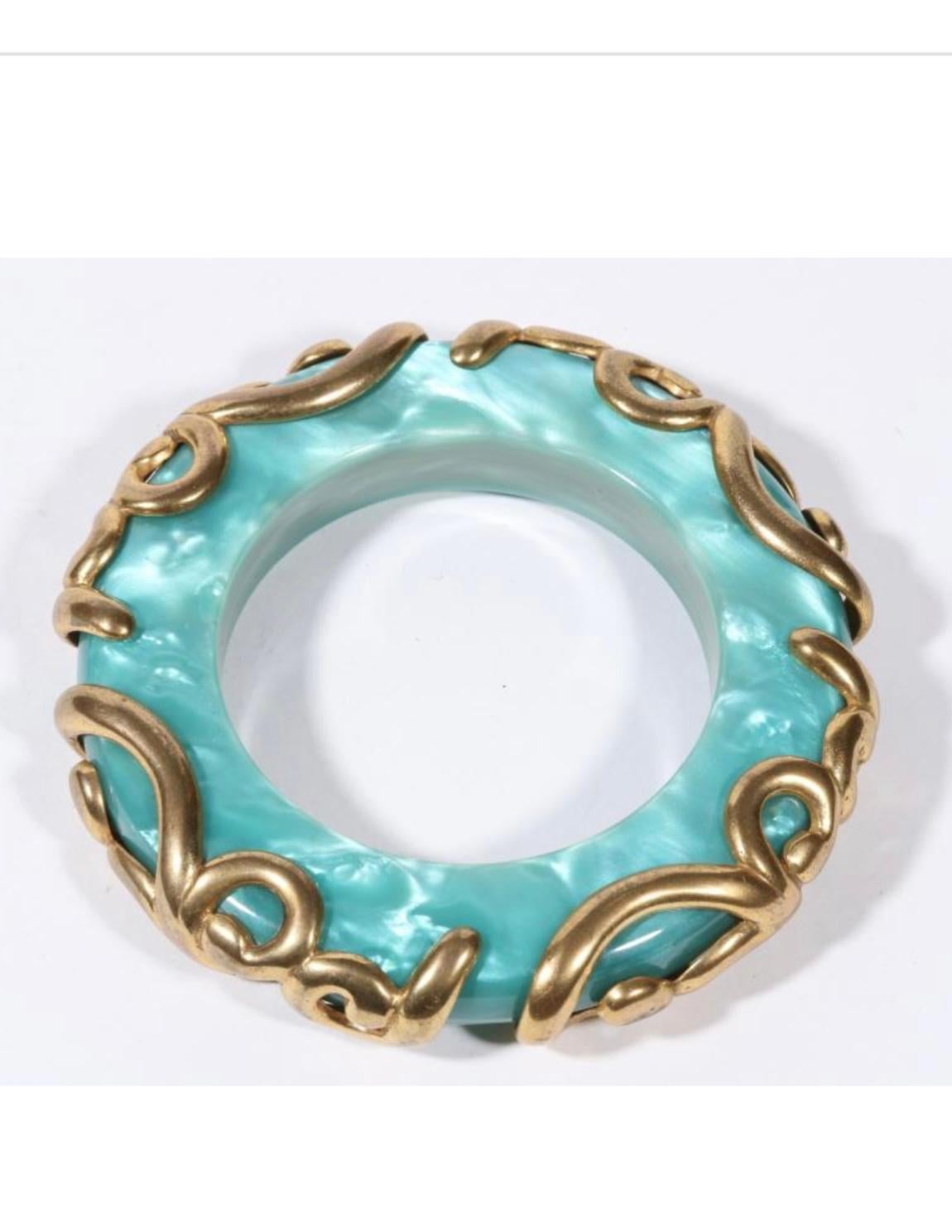 Date un capricho con esta magnífica pulsera brazalete Isabel Canovas de color azul caribeño nacarado con remolinos de latón dorado aplicados. El impresionante brazalete tiene una abertura interior de 2,5 cm de ancho y el interior mide 7,5 cm de