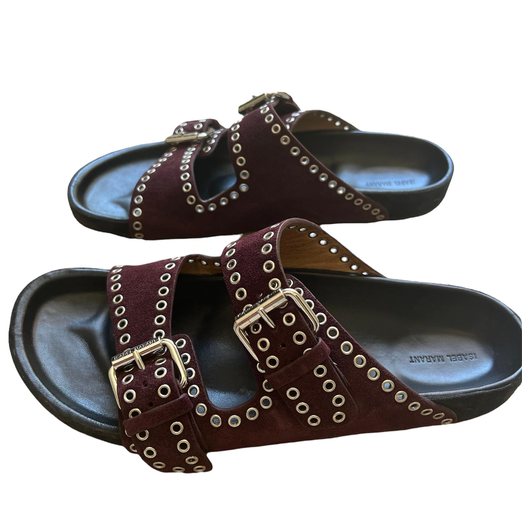 A pair of Isabel Marant Lennyo suede slides in burgundy.

​The sandals are generously dotted with the eyelets that appear oftenon Isabel Marant accessories. These polished grommets embellish smooth burgundy suede and add a rebel touch to the