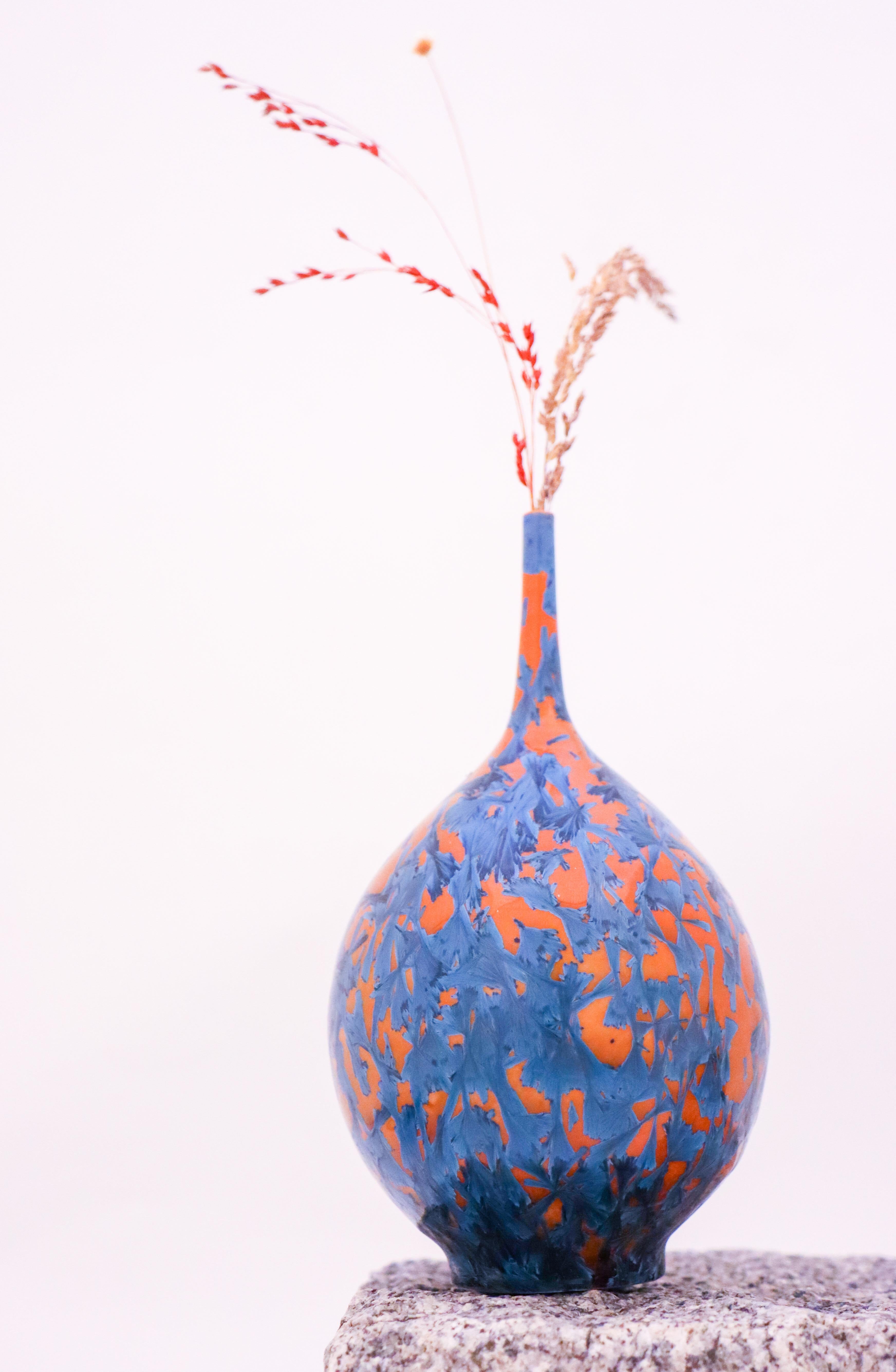 This striking vase by Isak Isaksson is a true masterpiece of contemporary design. Handmade in Sweden, it showcases a stunning abstract pattern in orange hues, finished with a glossy crystalline glaze. Measuring 16.5 cm in height, this vase is