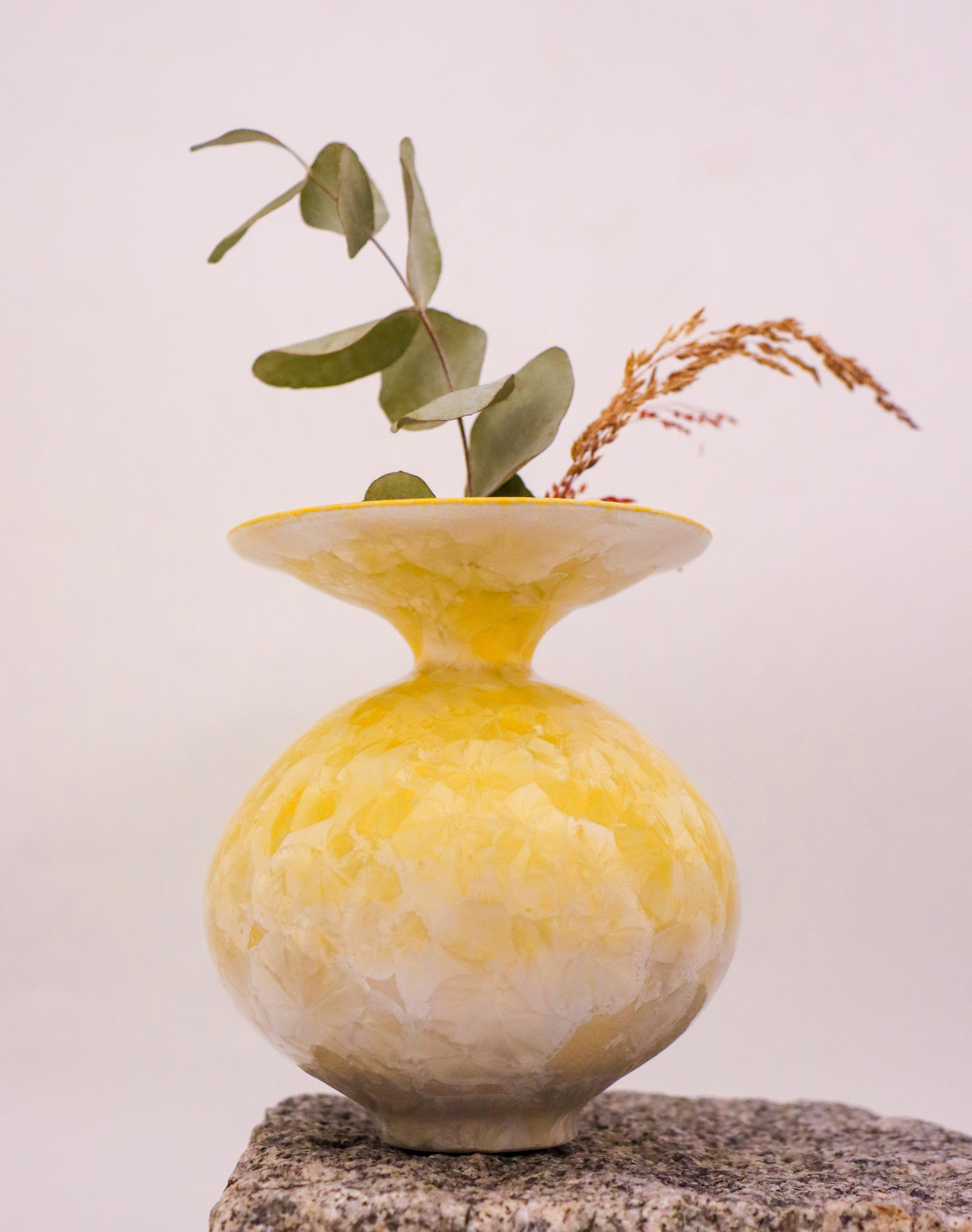 This Isak Isaksson vase showcases a stunning abstract design, with a glossy finish and a beautiful yellow color. The vase stands at a height of 12.5 cm and is made of ceramic, finished with a crystalline glaze. It is a contemporary piece of art