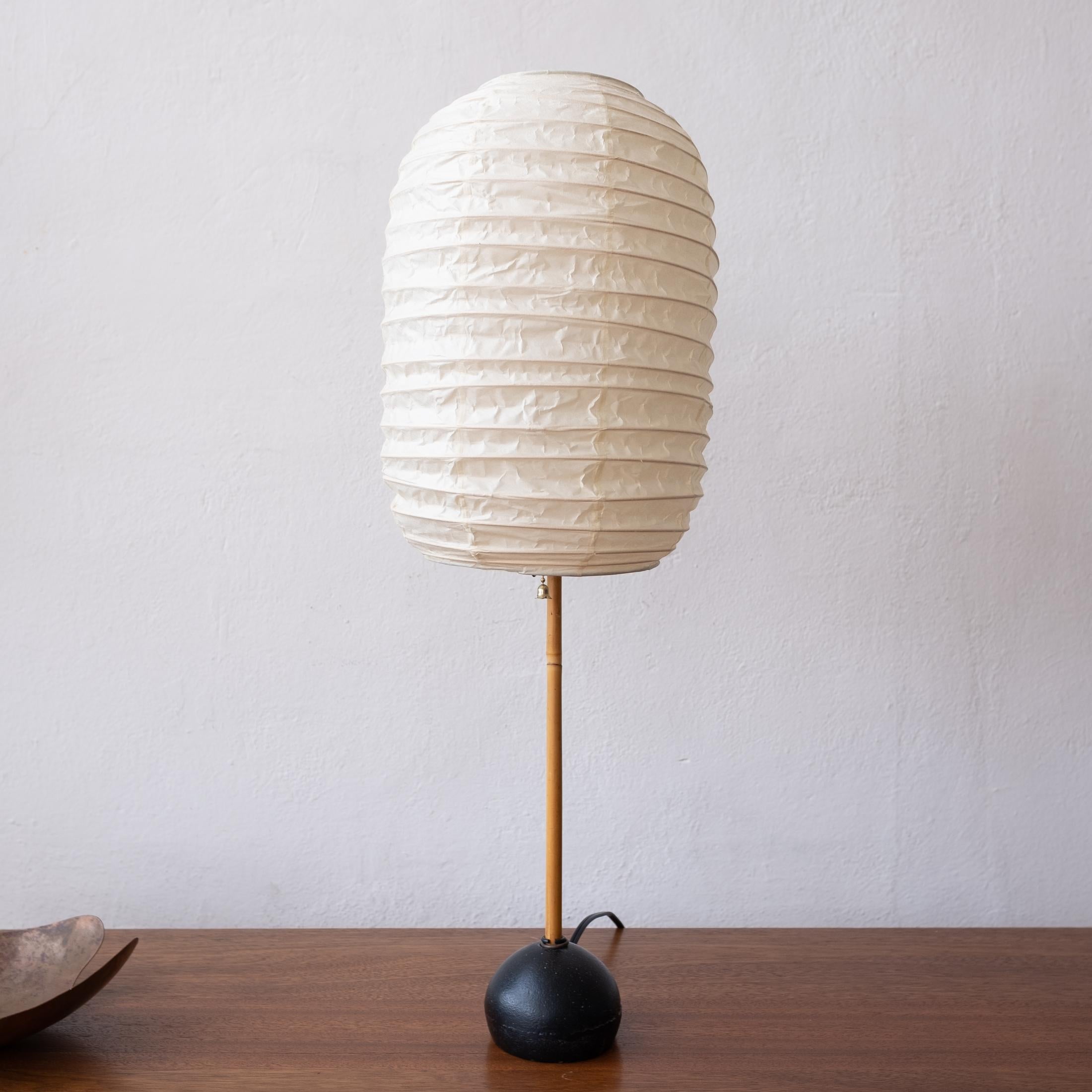 Isamu Noguchi Akari table lamp from the 1960s. Bamboo pole and iron rock form base. The paper shade has been replaced at some point with a genuine Noguchi signed shade. Made in Japan.