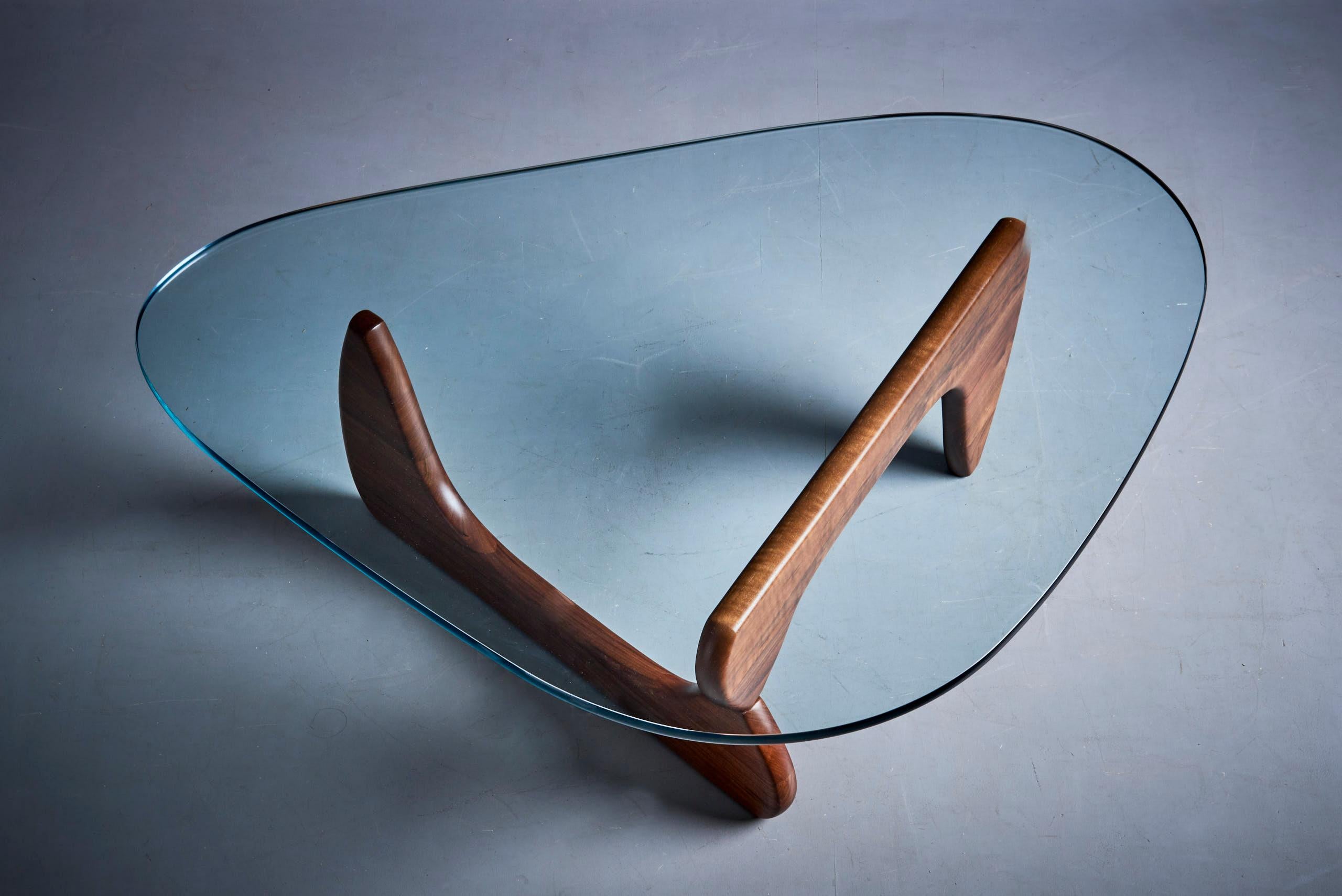 Der Couchtisch von Isamu Noguchi besteht aus zwei identischen, gespiegelten und versetzten Holzteilen, die eine stabile Basis für die dicke, 19 mm dicke Glasplatte bilden, die tropfenförmig und sanft abgerundet ist. Durch die geschickte Anordnung