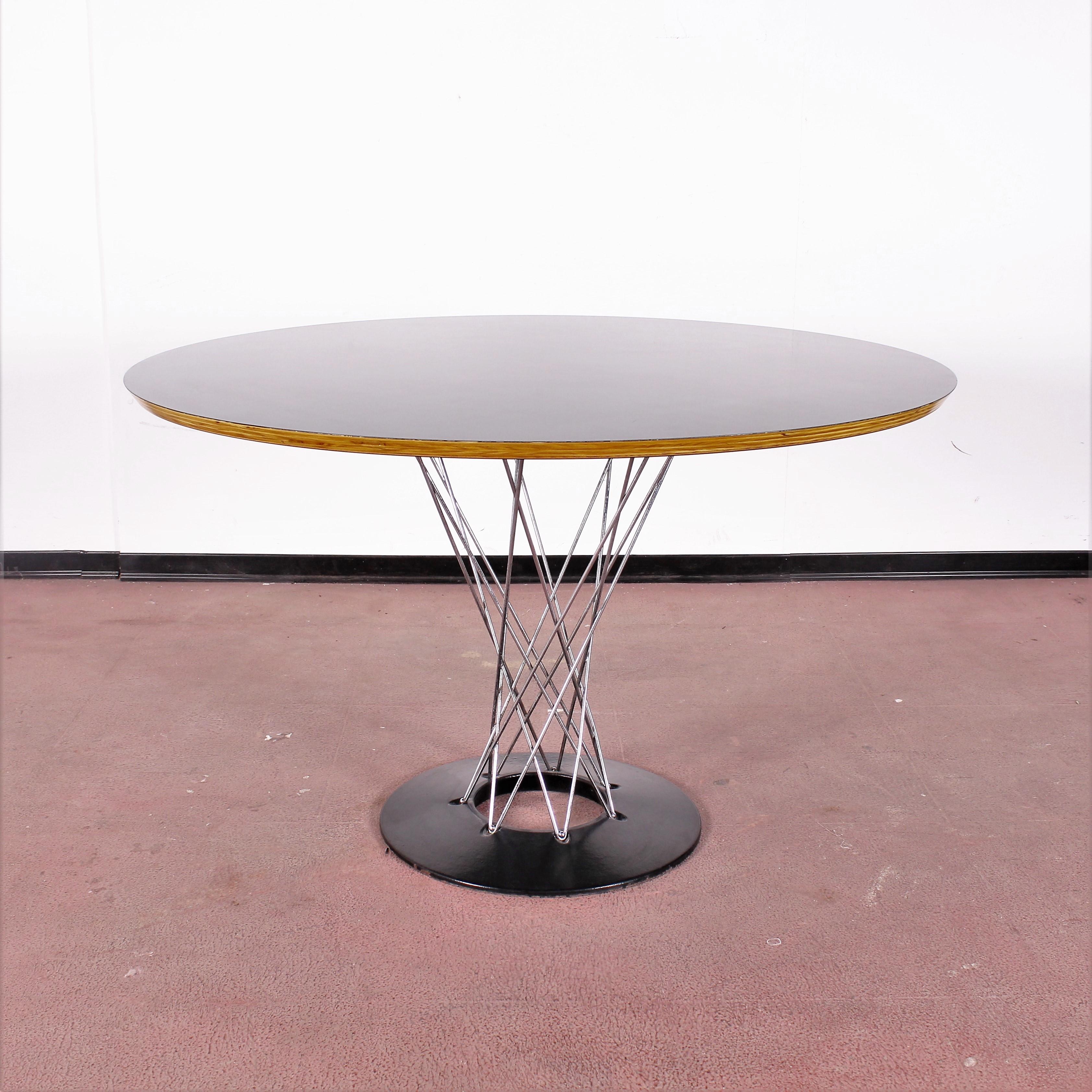 Beautiful dining table with circular top in plywood and black laminate. Feet in chromed twisted steel rods, screwed onto the circular base in black lacquered cast iron, by Isamu Noguchi for Alivar in 1980s.
Wear consistent with age and use.
   
