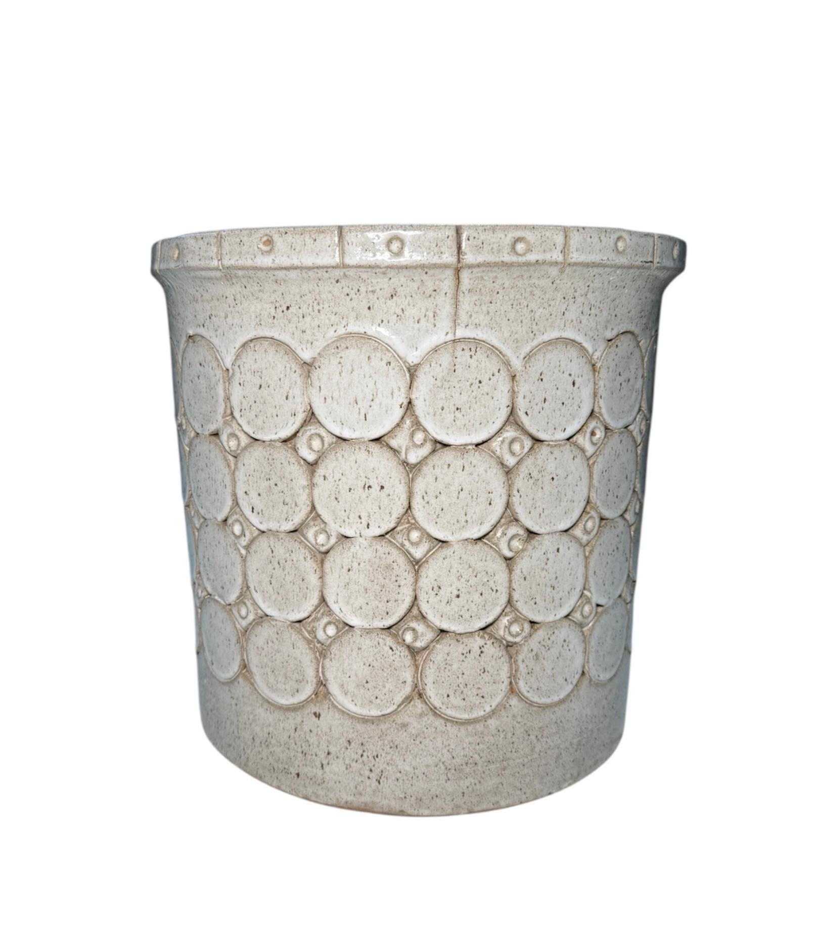 This is an Isla del Sol Puerto Rican Stoneware Planter. It depicts a round planter decorated with four rows of large circles alternated with three rows of small circles. The upper border is also adorned with rectangles with a central circle. It is