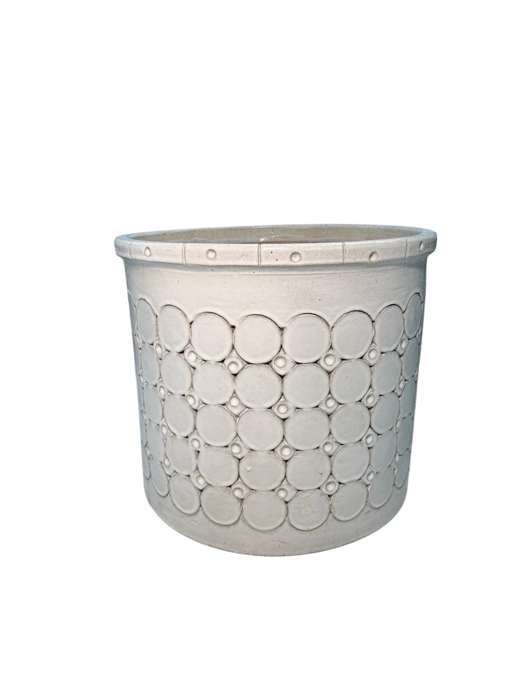 This is an Isla del Sol Puerto Rican Stoneware Planter. It depicts a round pearl color planter decorated with five rows of big circles alternated with four rows of small circles. It is a heavy planter and its weight is approximately 60 pounds. This