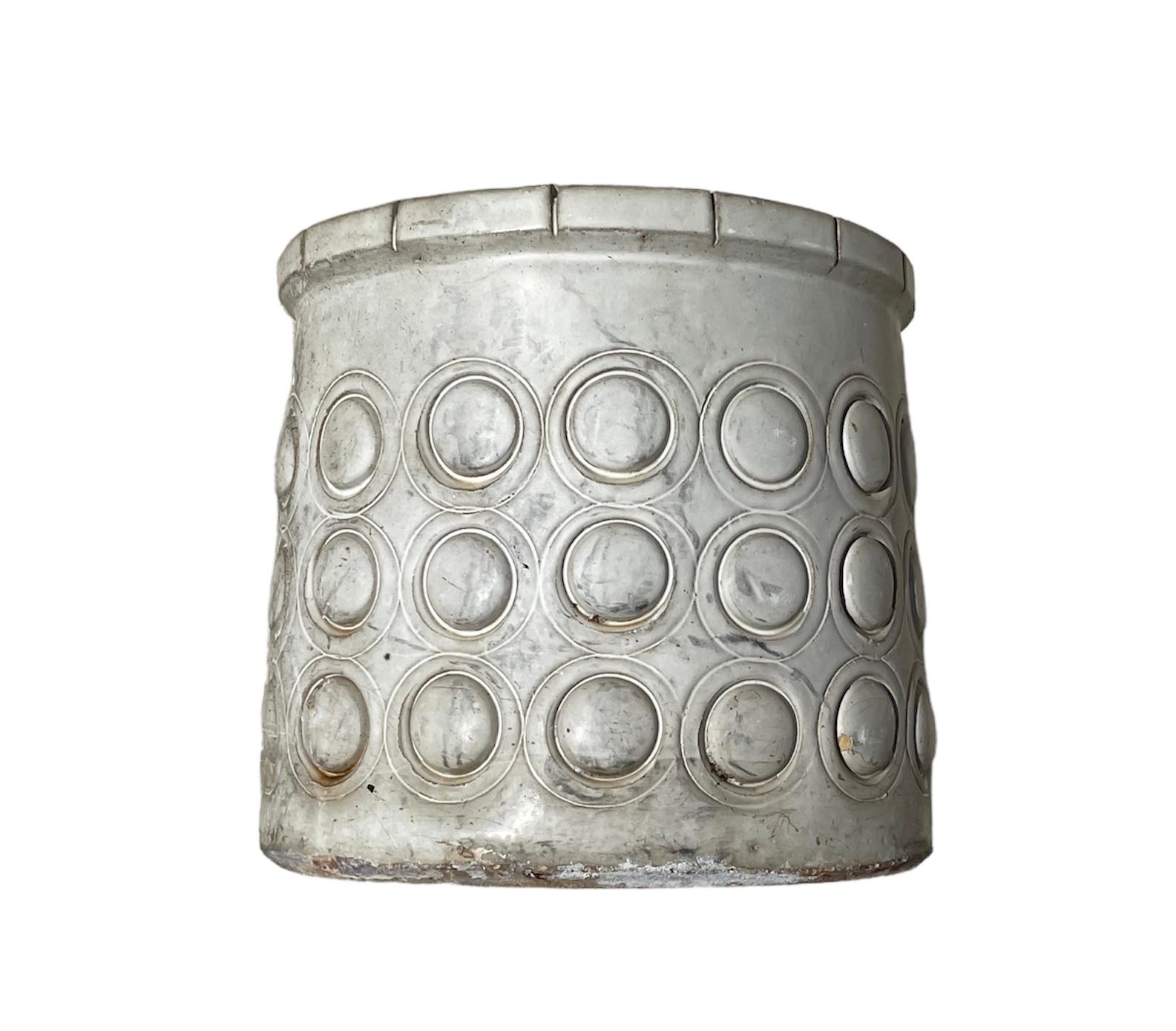 This is an Isla Del Sol Puerto Rican Stoneware Planter. It depicts a heavy round planter painted light grey pearly color and decorated with three rows of convex hemispheres. The upper border is decorated with rectangles.
