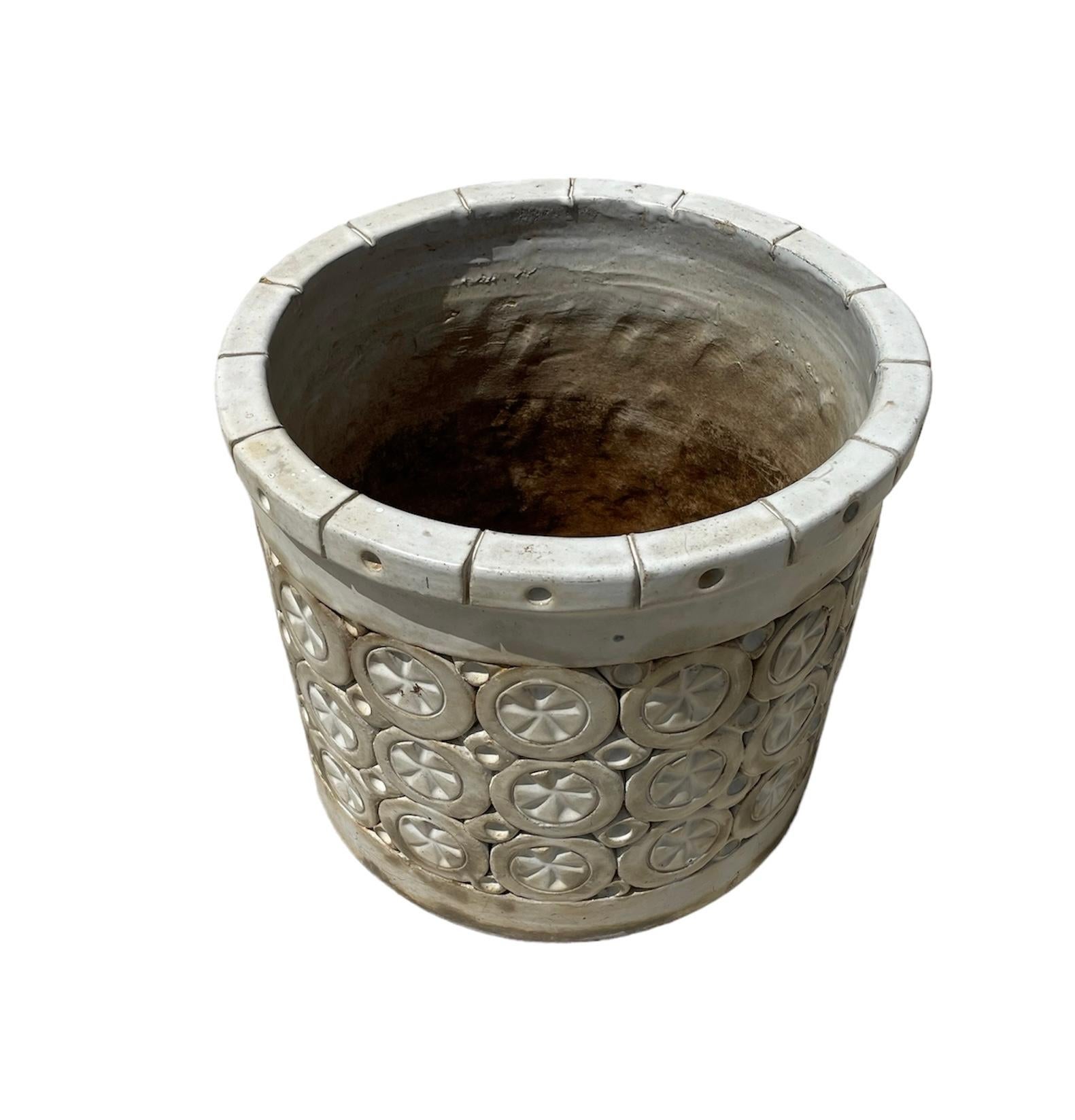 This is an Isla Del Sol Stoneware Planter. It depicts a heavy round planter decorated with three rows of circles adorned in the center with stars alternated with four rows of squares with concave hemispheric centers. The upper border is also