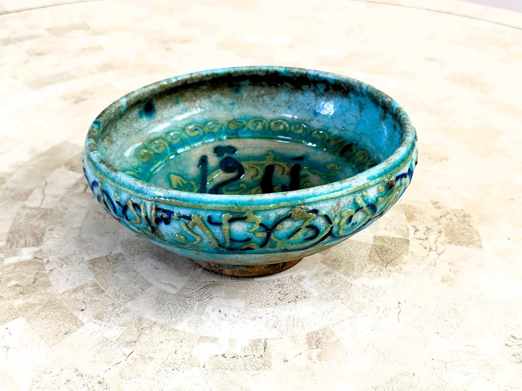 An Islamic glazed ceramic bowl with inscription attributed to Raqqa ware, produced during the Ayyubid dynasty (12-13th century) in the town of Raqqa in nowadays northeastern Syria. The bowl figures a generous volume with a rounded body tapered to