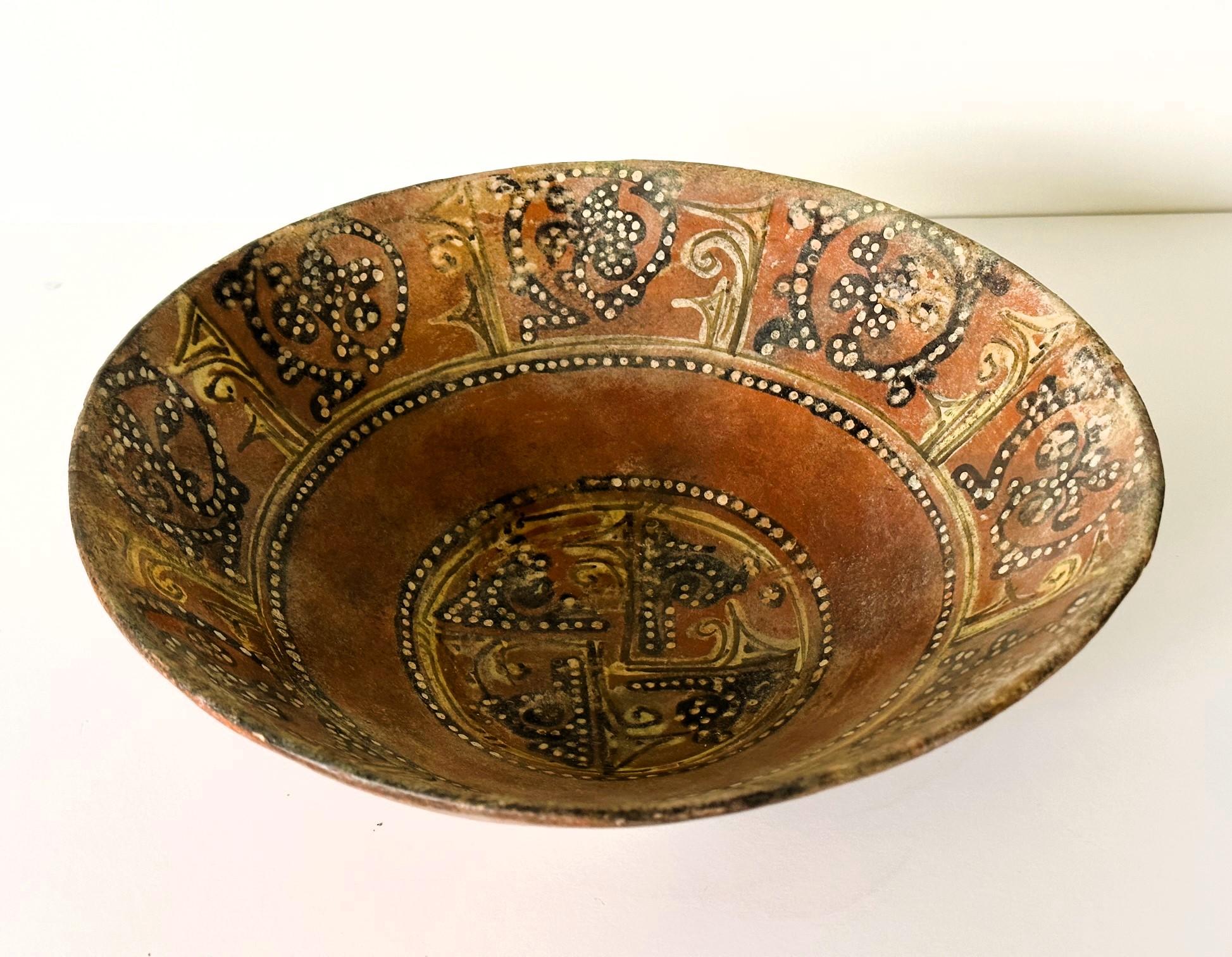 A deep and wide earthenware bowl supported on a foot ring decorated with slip paint from Nishapur 11th century under the Seljuk Empire (in nowadays Iran). This bowl features a thinly pottered wall covered in an ocher color slip background. On top of