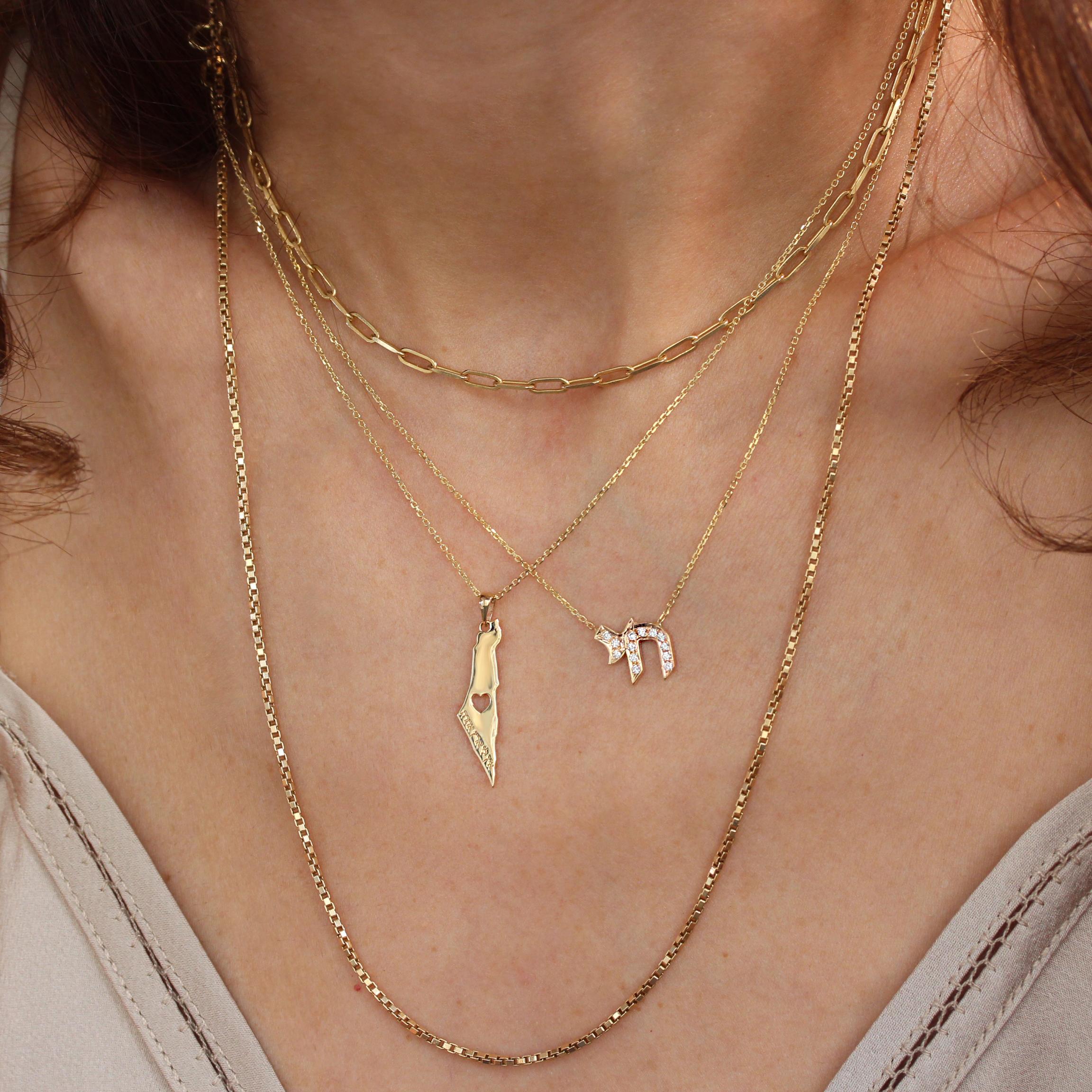 Am Israel Chai gold Pendant Necklace featuring the map of Israel intricately crafted with a heart-shaped void, symbolizing love for the nation. The pendant is designed with an engraved Hebrew inscription, expressing a deep connection and pride. This