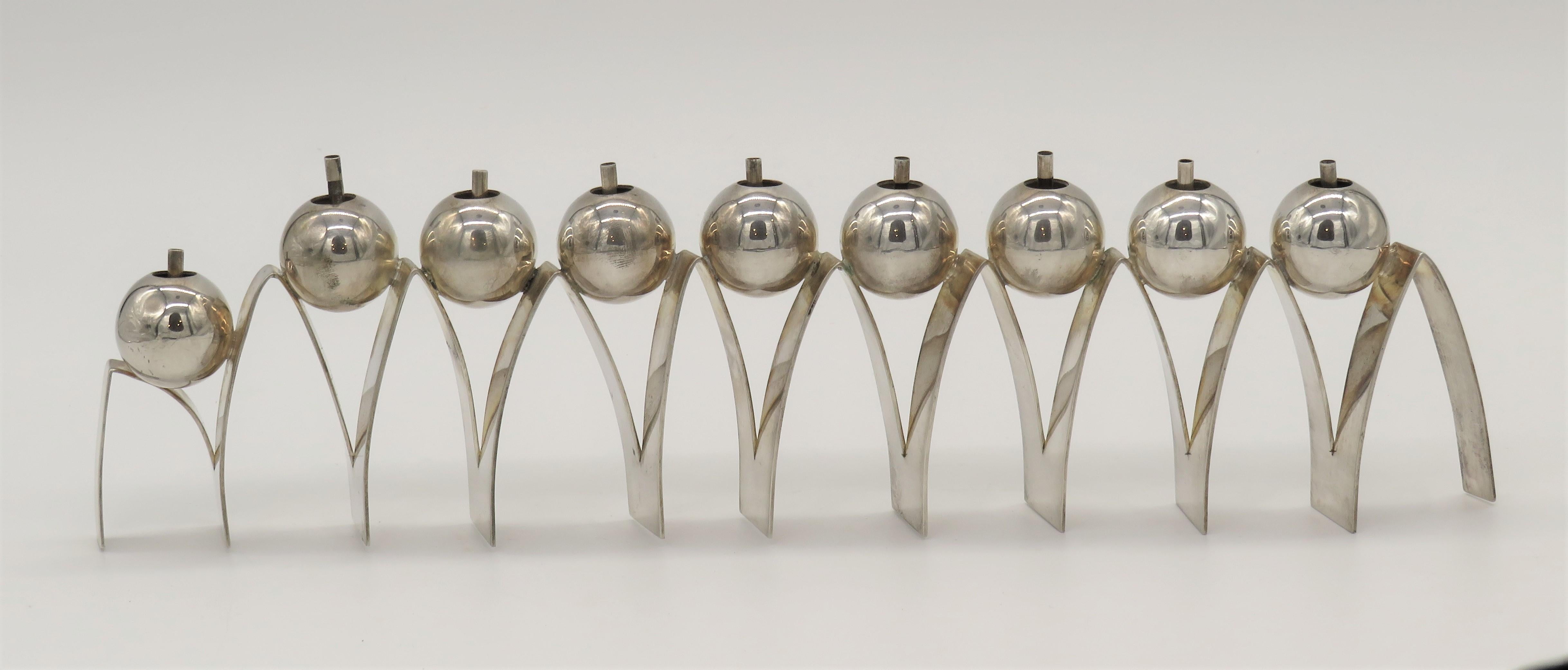 Israeli silver hanukkah lamp by Arie Ofir features nine balls supported by a zig zag base. The stunning silver Hanukkah lamp is for use with oil and candle wicks. Signed and stamped by Arie Ofir with silver hallmarks are seen. 

The Hanukkah lamp
