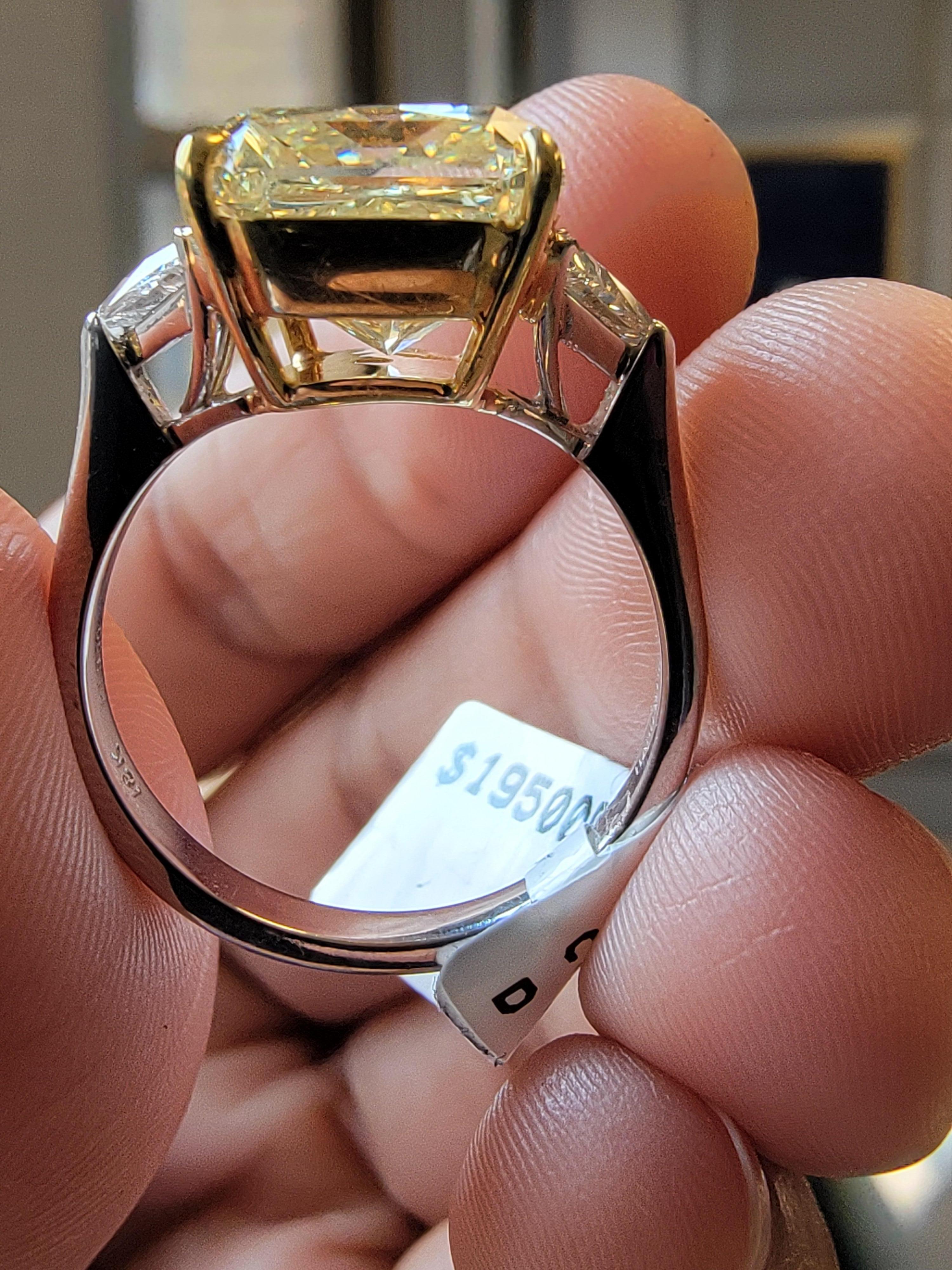 The ring itself features, Large radiant natural fancy yellow diamond. Stone is set with two white step-cut trapezoid diamonds. This central stone is surrounded by a  of smaller white diamonds that enhance its brilliance and draw attention to the