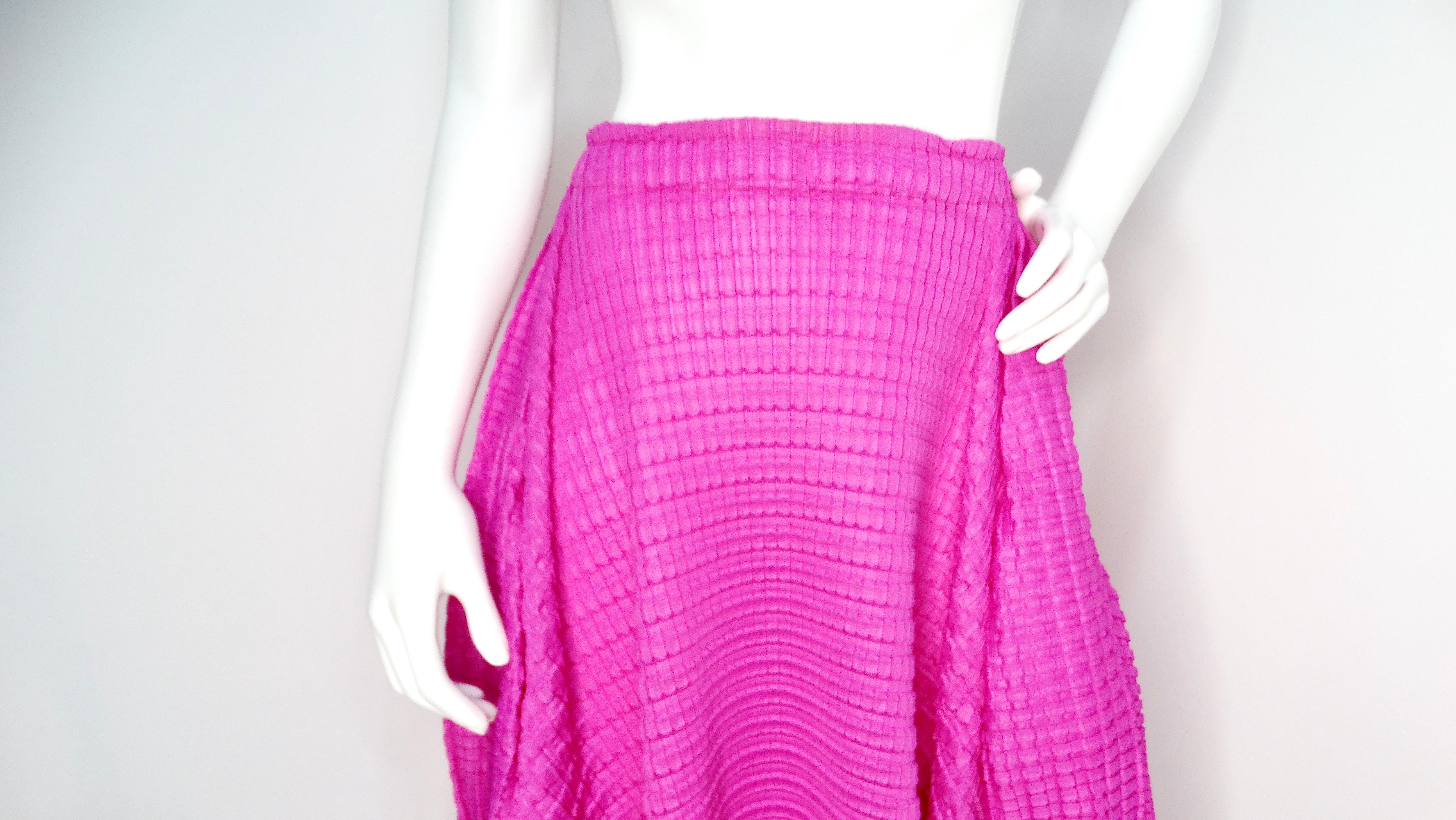 The Issey Miyake 1990s Pleats Please Midi Skirt in a vibrant magenta hue is a stunning example of the designer's innovative approach to fabric manipulation. Featuring small, delightful pleats that create the illusion of bubbled mini squares, this
