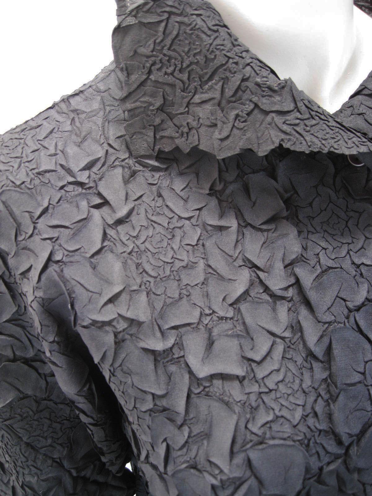Black textured blouse by Issey Miyake. While somewhat abstract, I feel this denotes a floral pattern.

Crinkled texture with lots of stretch.

Button down with stand up/fold over collar.

Fabric is Polyester.

Marked size 2.

This item is in