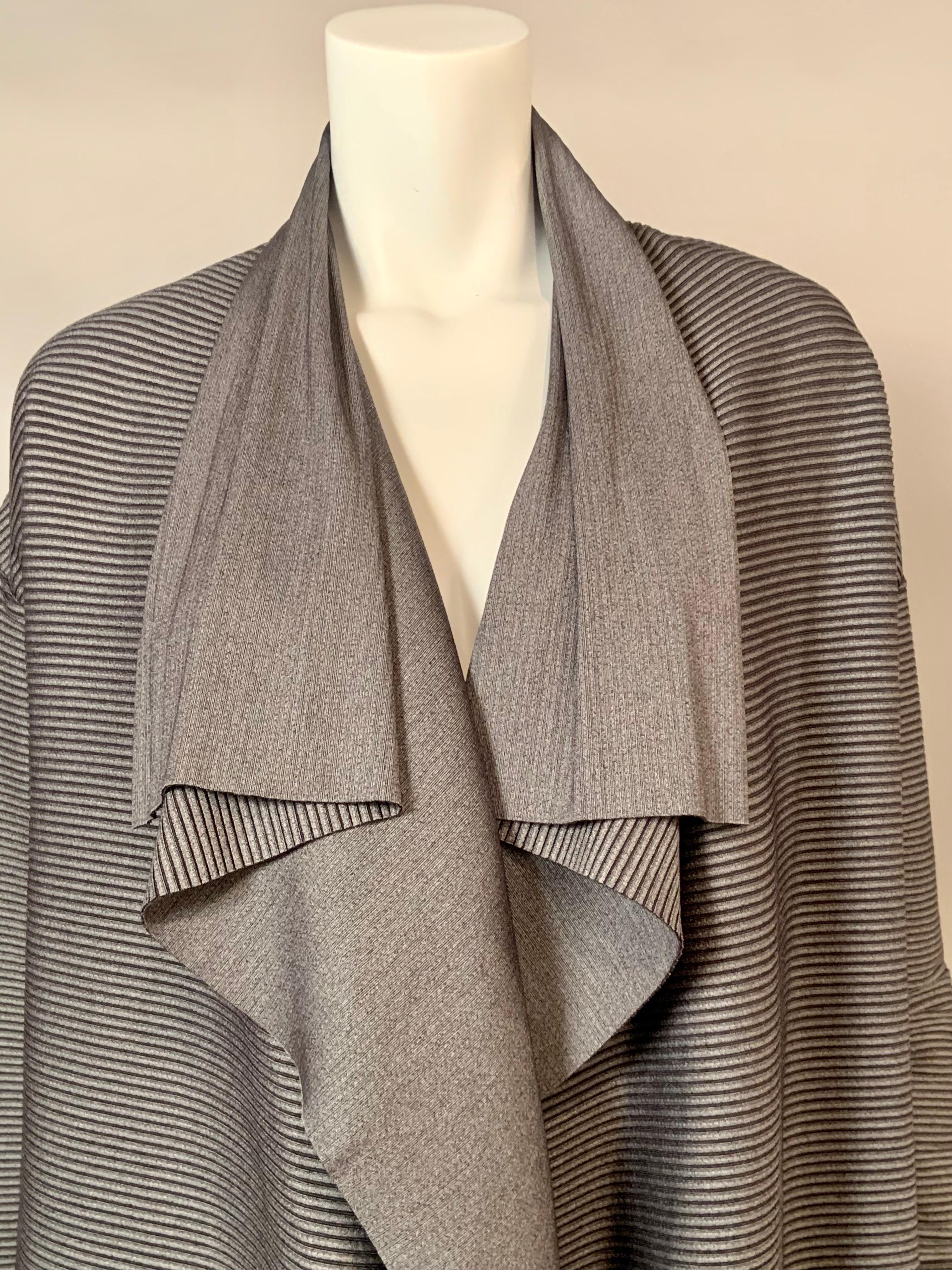 Questo cappotto grigio leggero disegnato da Issey Miyake è realizzato con un tessuto molto interessante.  È semitrasparente, le strisce scure sono trasparenti e il tessuto si estende in molte direzioni.  L'ampio colletto drappeggiato, i polsini e