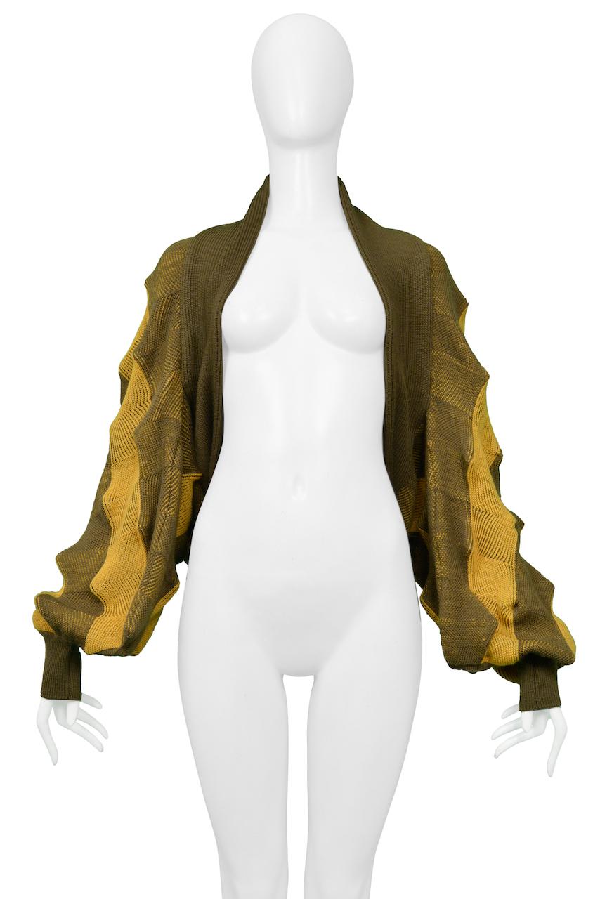 Resurrection Vintage freut sich, einen gold-olivfarbenen Bolero-Pullover von Issey Miyake anbieten zu können, der die kultigen Beulen der Eierkartonform aufweist. 

Issey Miyake
Größe: Einheitsgröße 
Stricken
Ausgezeichneter Vintage By