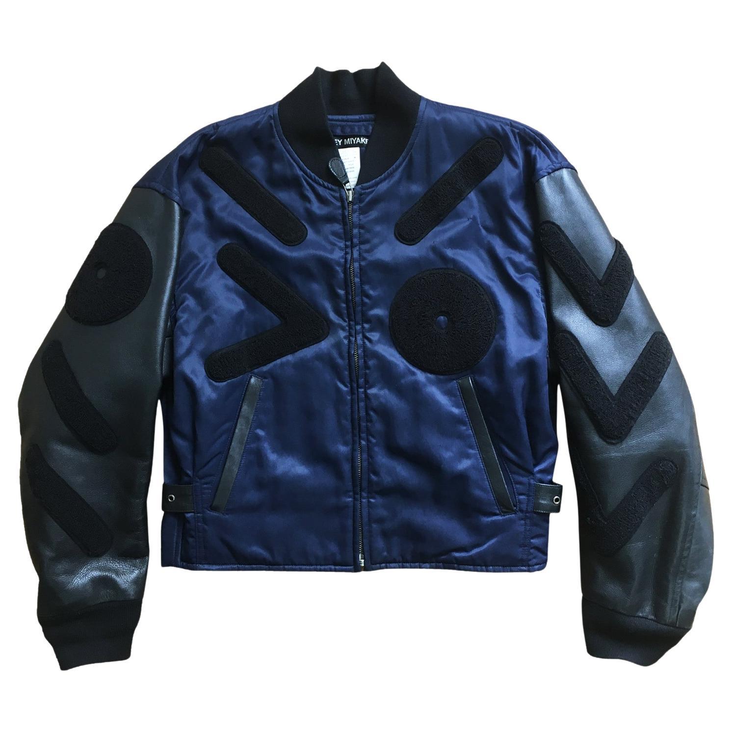 Issey Miyake navy and black patch-appliqué bomber jacket from SS 1994 collection. 
Embroidery detailing at front, sleeves and back with Patch-appliqué with leather on sleeve and pocket
opening.
Lining: cotton 100%, wool 100%
Outer: nylon 100%

Size