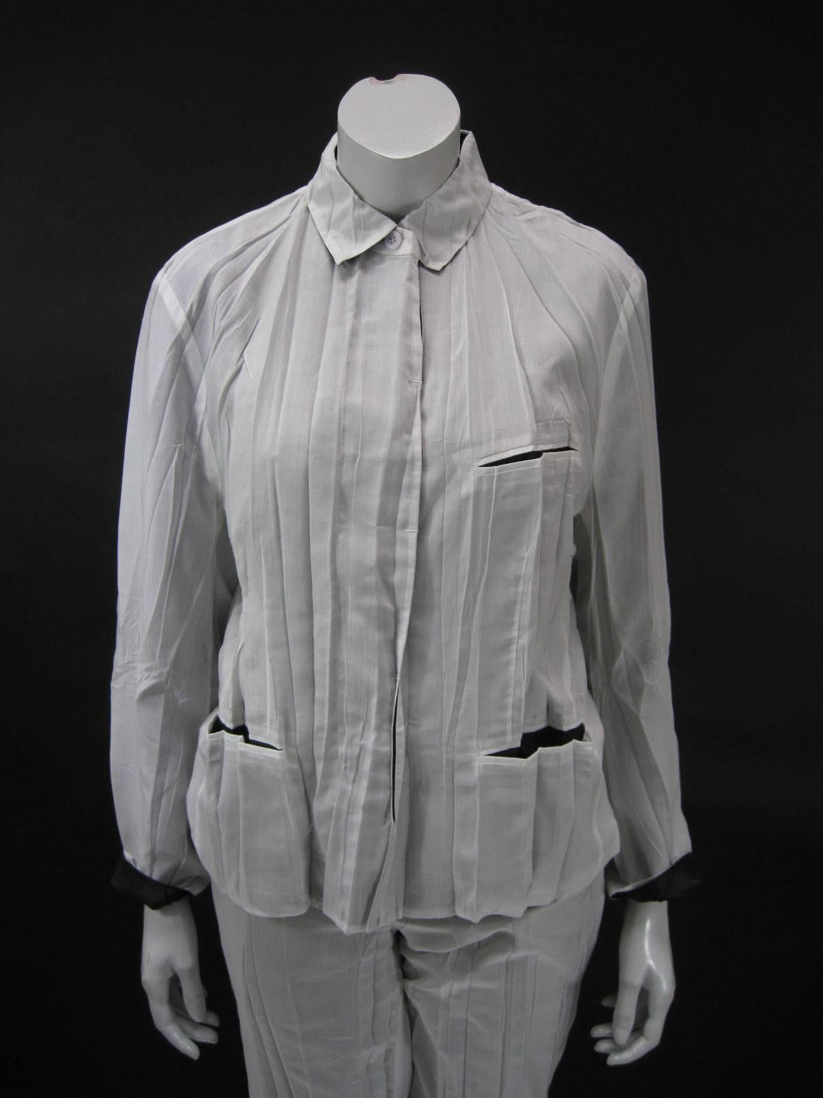 Chaqueta plisada Issey Miyake con pantalones.

Tejido de dos capas: blanco roto semitransparente sobre negro. 

El top tiene 5 botones ocultos, un bolsillo en el pecho y dos bolsillos en la cadera con forro de contraste.

Los pantalones tienen aros