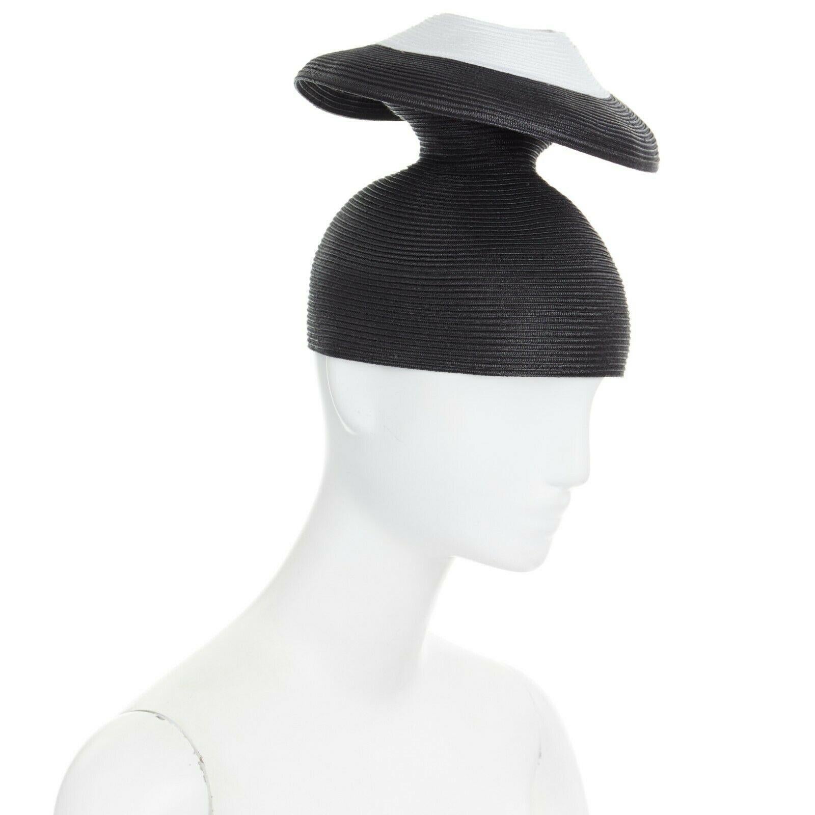 ISSEY MIYAKE PLEATS PLEASE
Black raffia straw knit. White circle at top. Architectural dual layered design. Statement party hat. Grosgrain trimmed along lining. Made in Japan.

CONDITION
New without tags.
