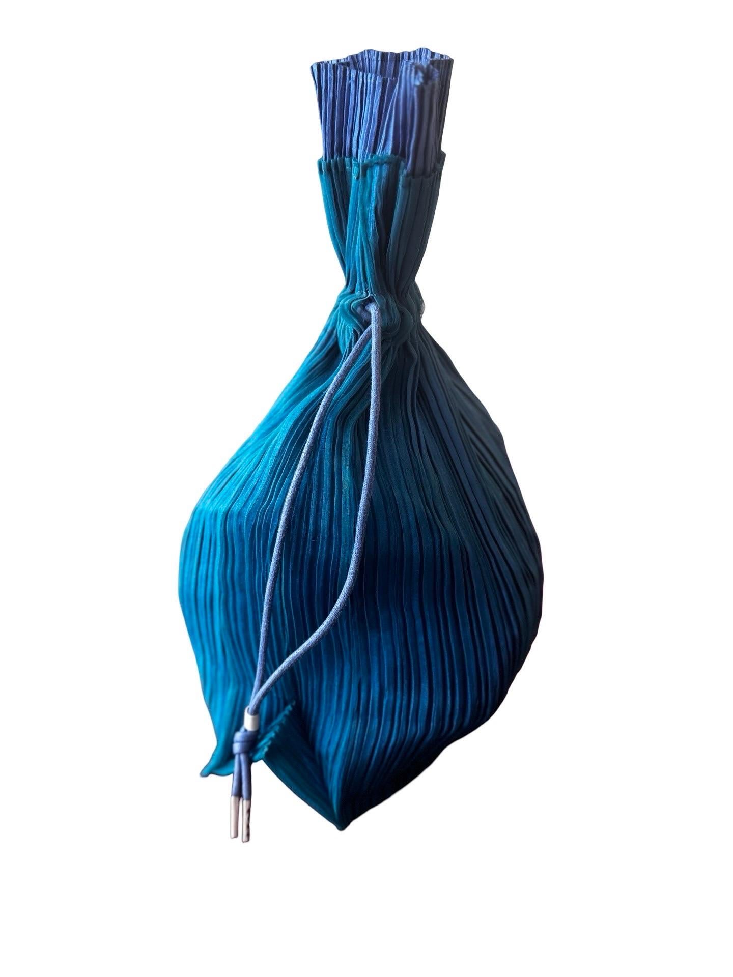 Issey Miyake main line plisse bag in double layer pleated organza in a teal color on top and a cornflower blue for the internal layer.  Same blue for the drawstrings.   Lays flat with minimal or no contents and sits up straight on the base with more