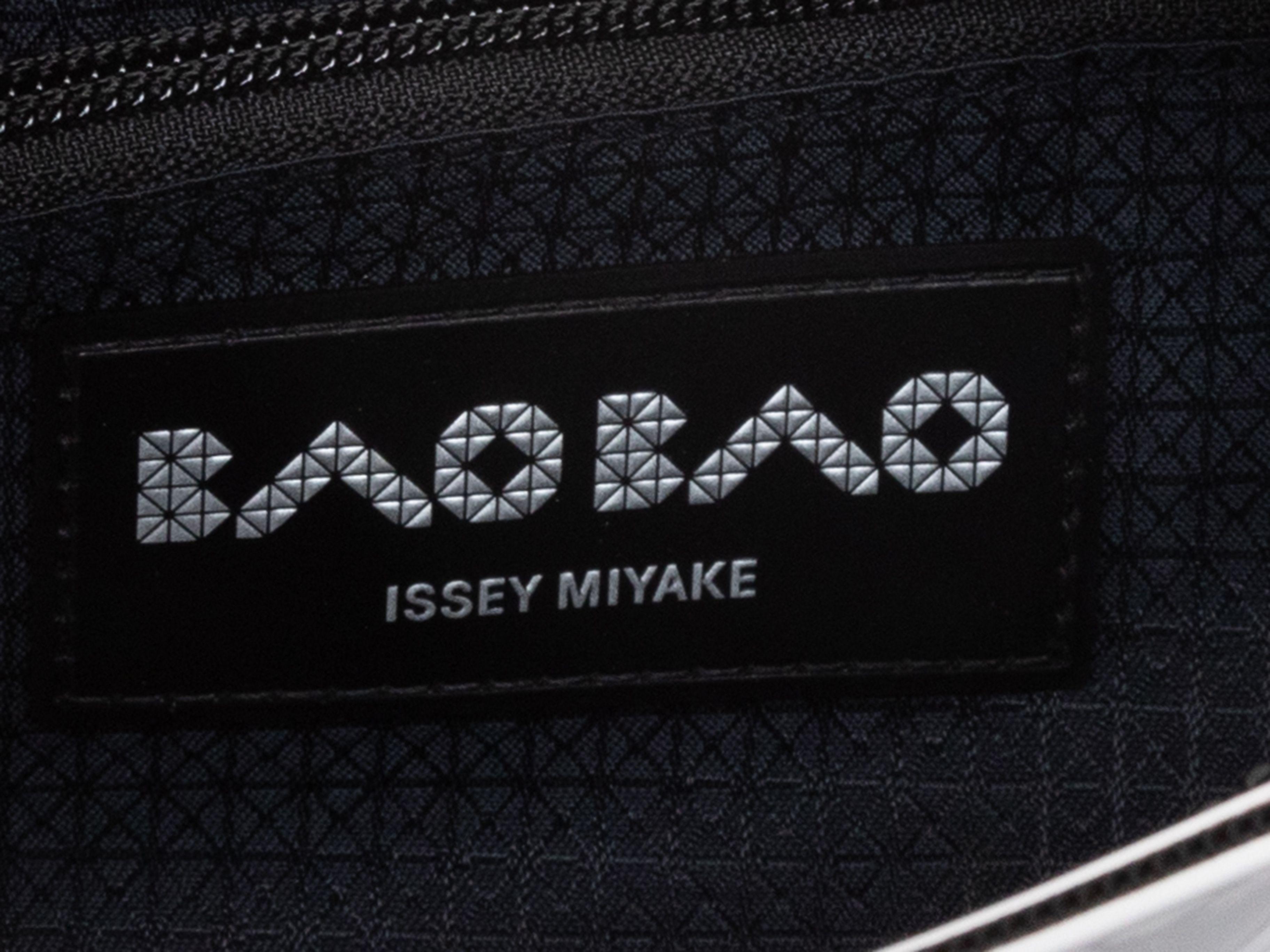 Product Details: White & Black Issey Miyake Bao Bao Crossbody Bag. This Bao Bao bag features a mesh and polyvinyl body, silver-tone hardware, a single flat crossbody strap, and a top zip closure. 9.5