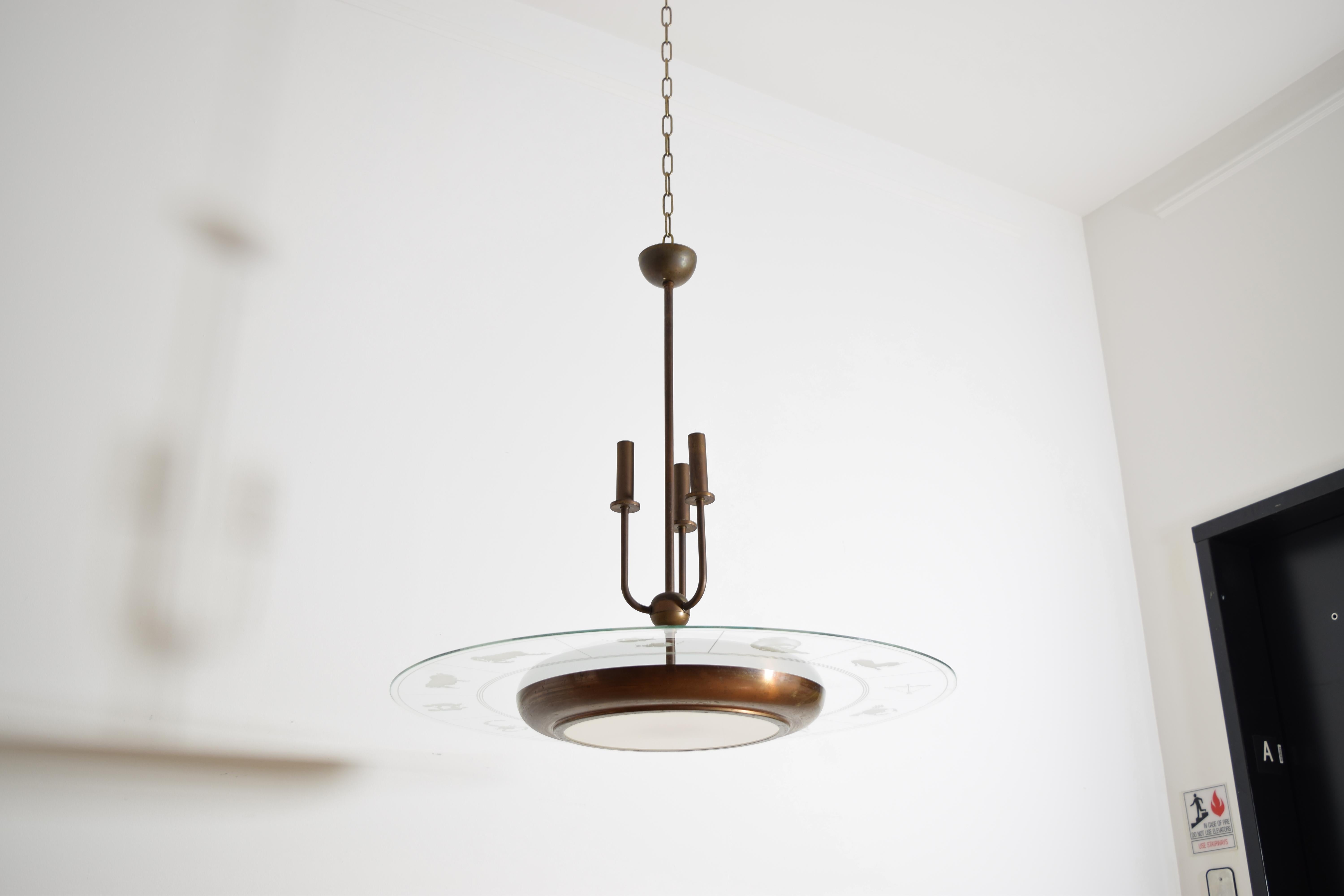 avendo  un'asta centrale in ottone con tre luci di ribalta e tre luci laterali nascoste nella parte inferiore, appena sopra l'inserto in vetro opaco, il grande disco di vetro originale poggia sulla cornice in ottone ed è inciso con i segni dello