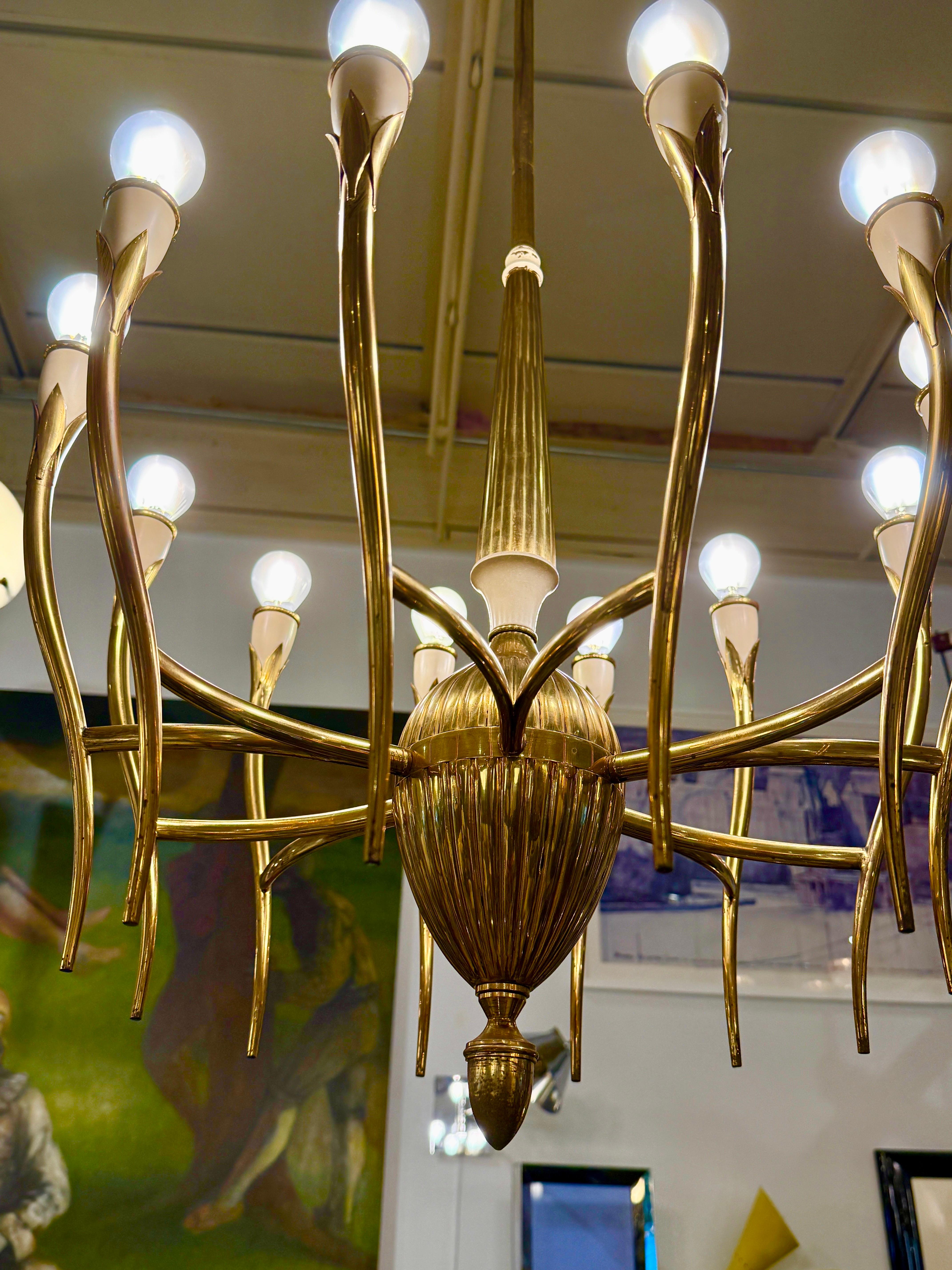 Designed by Oscar Torlasco, this rare Italian brass 12-arm chandelier from the 1940-1950s, featuring tulip style twelve slender and sensuously curved brass arms with a satin finish and off-white lacquered socket covers. Original brass E14 sockets.