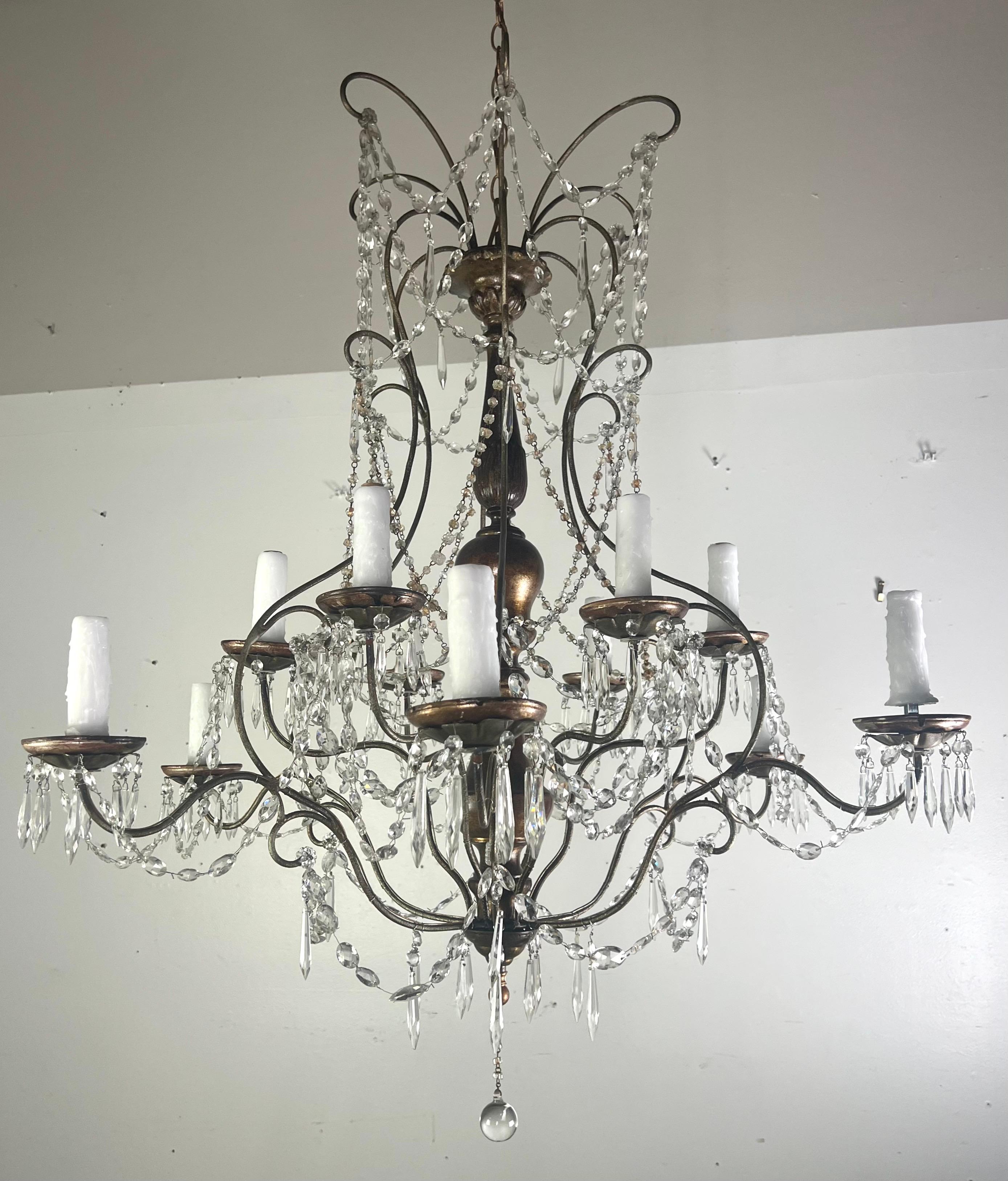 Italian (12) light gilt wood & crystal chandelier.  The (12) arms curve outward from a center gilt wood column, each supporting a drip wax candle cover for light bulbs.  The chandelier is adorned with clear crystal drops and garlands of beaded