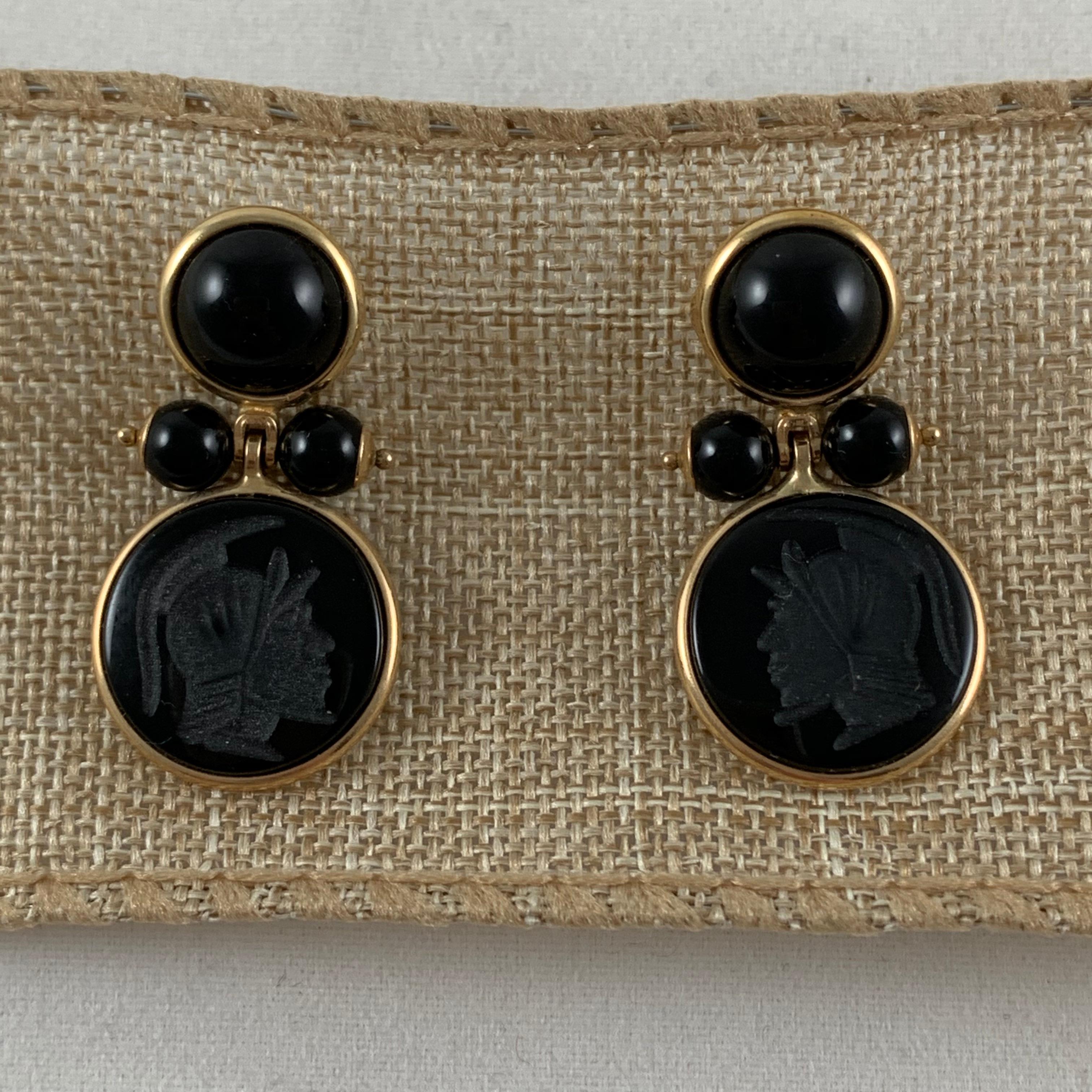 From Italy, a pair of 14-karat gold framed earrings with black onyx cabochons, beads, and carved armorial intaglios. Posted with backs.

The upper bezels hold flat back cabochon cut, domed onyx stones, terminating with two pinned and capped onyx