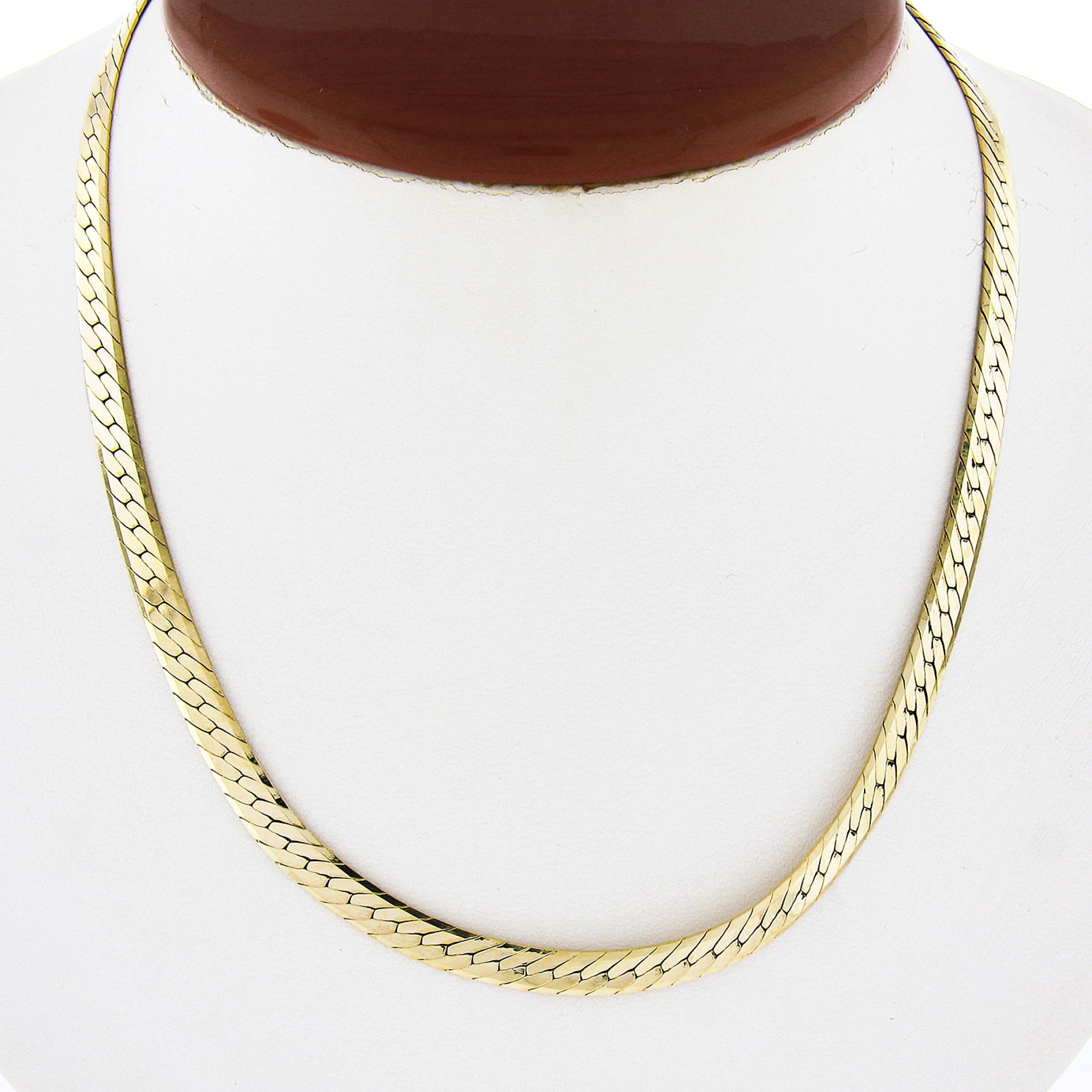 This well made chain necklace was crafted in Italy from solid 14k yellow gold and features a thick, flat, herringbone link with a high-polished finish throughout that gives this piece a very attractive and shiny look. The chain measures 16 inches in