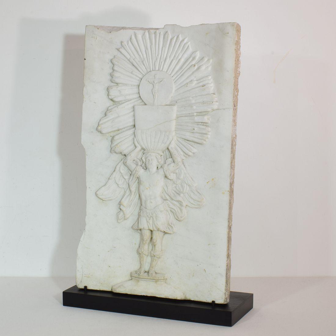 Unique and beautiful weathered white marble panel representing an angel holding a chalice with sunburst and crucified Christ figure . Well detailed, Italy, circa 1650-1750. Weathered, small losses.