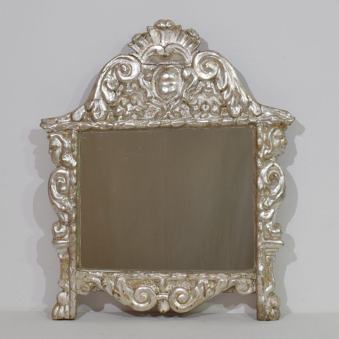 Superbe miroir à feuilles d'argent sculpté à la main au XVIIe/XVIIIe siècle. Sur les côtés du miroir, on peut voir deux têtes d'ange sur des boucles baroques et des pieds griffus. 
Italie, vers 1650-1750, altéré, petites pertes et réparations