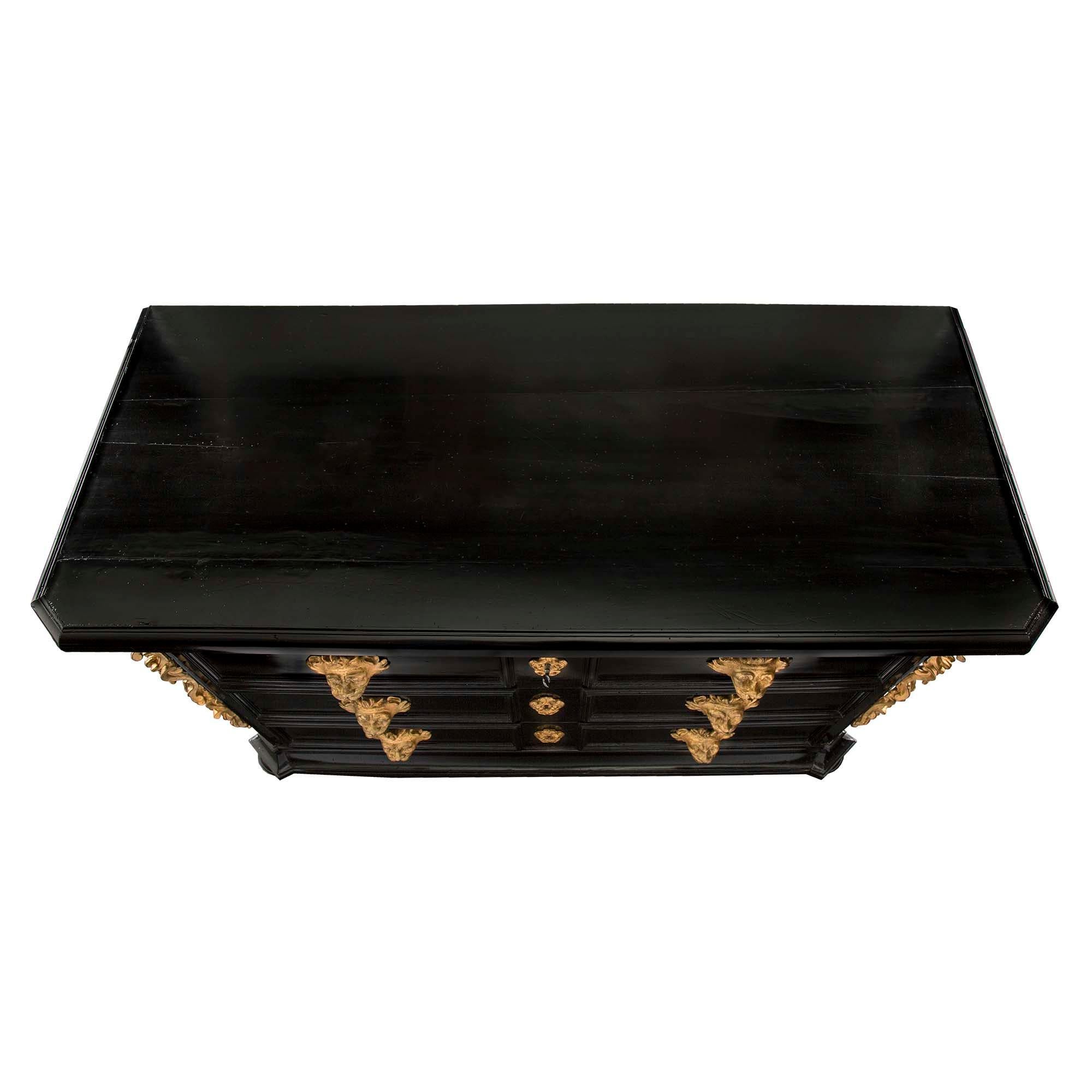 A most handsome Italian 17th century Baroque period ebonized fruitwood and giltwood chest, from Florence. The four drawer chest is raised by bun feet below a mottled border. At the center are three wide drawers, decorated with sensational detailed