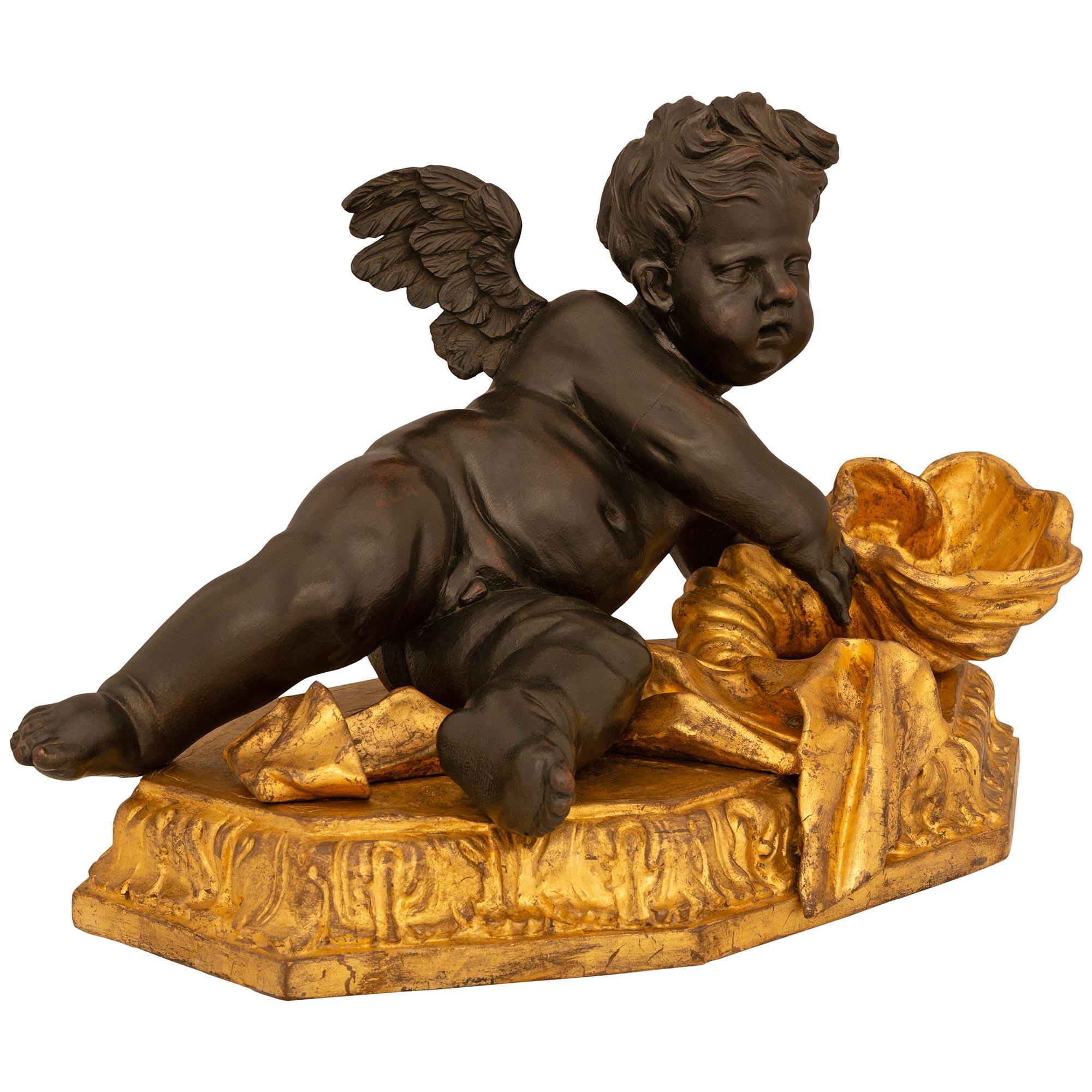 An elegant and extremely decorative Italian 17th century Baroque period Giltwood and patinated wood Putti statue. The statue is raised by a Giltwood plinth with a Coeur-de-Rai carved edge. Above the plinth is a patinated wood winged putti posing