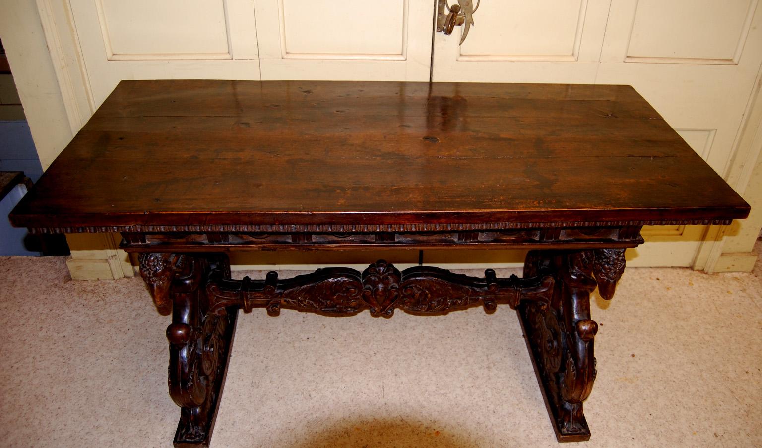 Italian 17th century carved walnut center table with scrolled carved pedestal ends, central carved stretcher and three plank thick walnut top with applied carved frieze.  The pedestal ends center on a female figure, framed by strongly carved rams