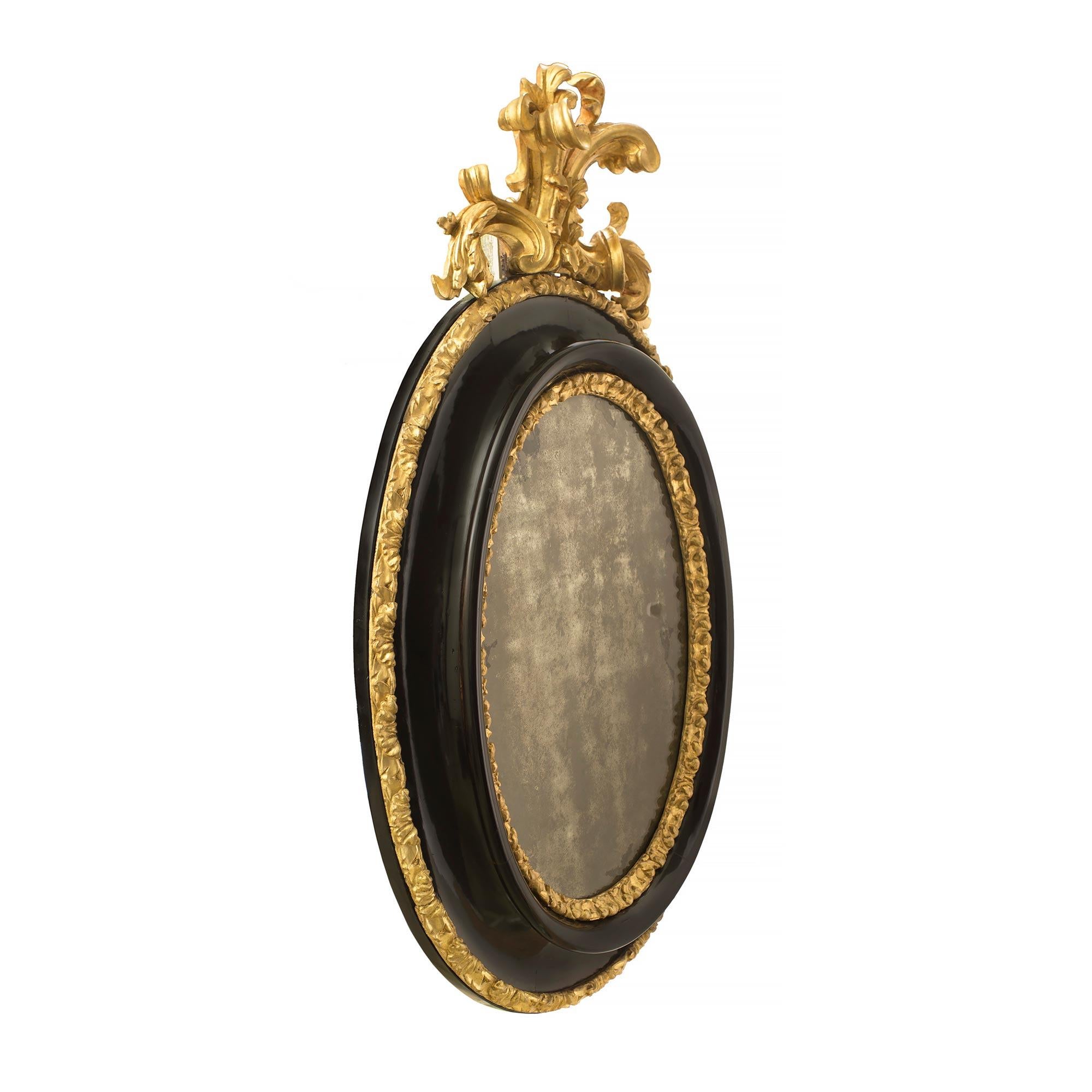 A striking Italian 17th century giltwood and ebonized fruitwood Florentine mirror. The original oval mirror plate is framed within two finely carved foliate giltwood bands centered by a mottled ebonized fruitwood border. All below the impressive