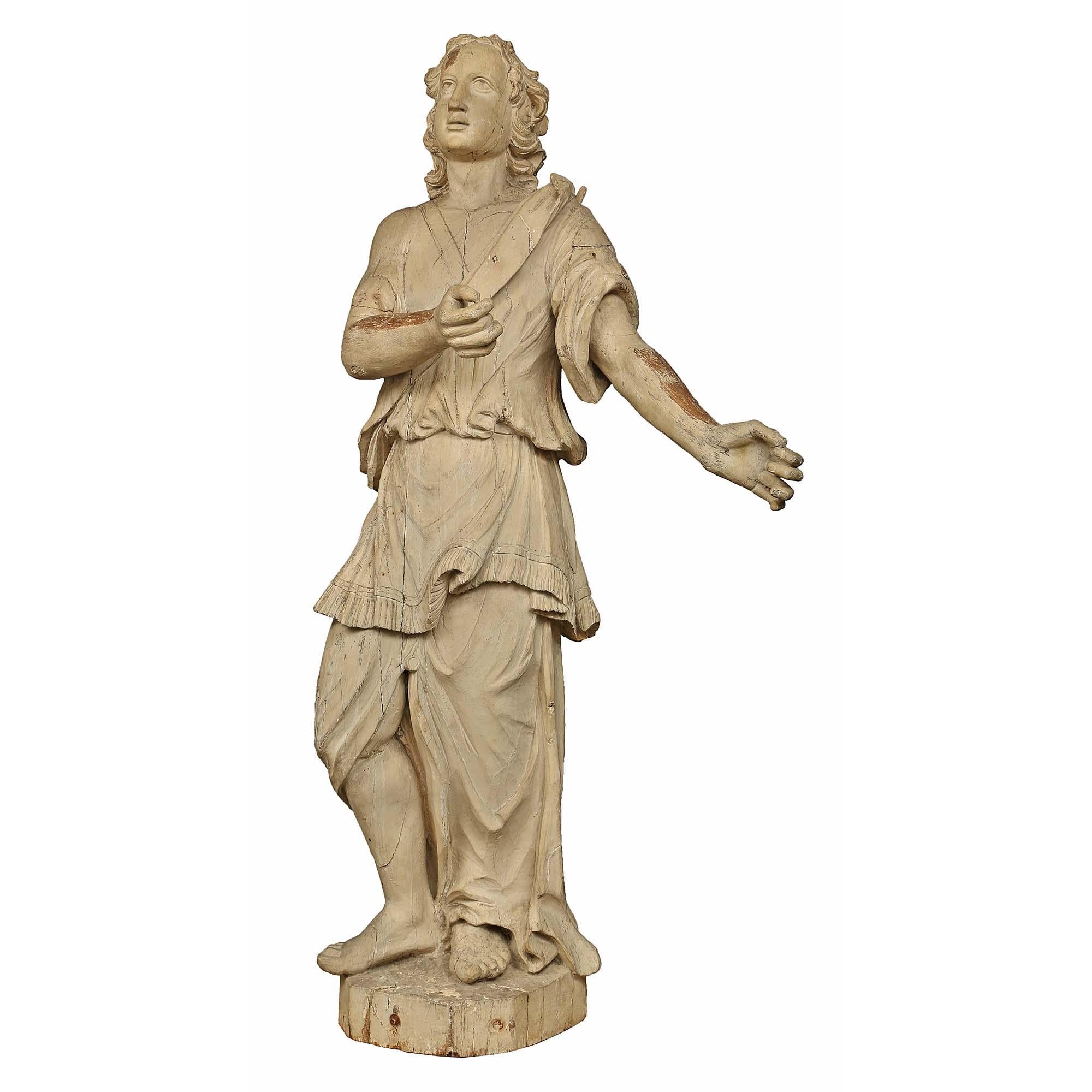 A wonderful and charming Italian 17th century patinated wood carved statue of an angel. The captivating angel is raised by a circular base and dressed in an exceptionally carved period robe. The charming angel, with finely carved long hair, stands